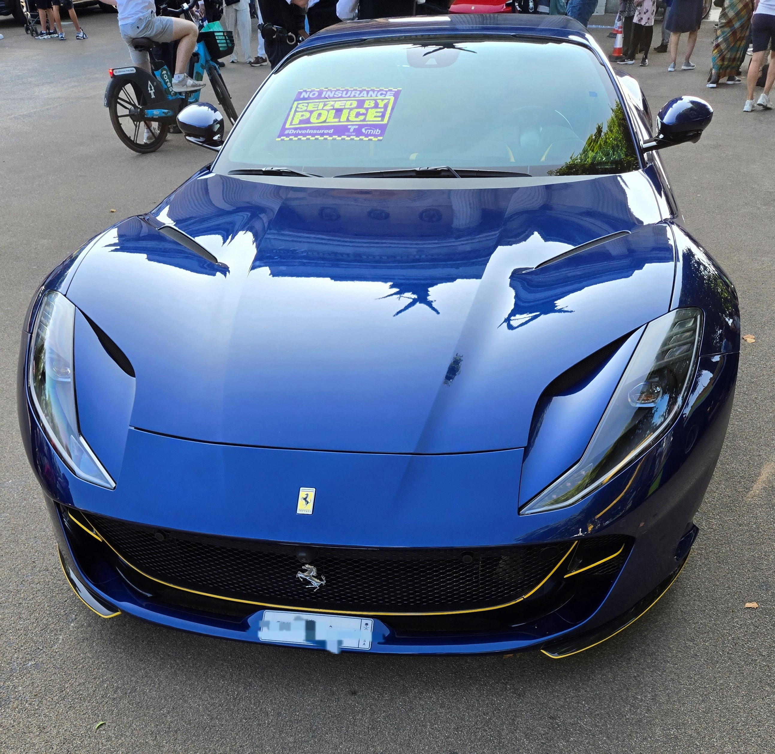 A blue Ferrari with a stick on the windscreen reading 'No insurance, vehicle seized by police'