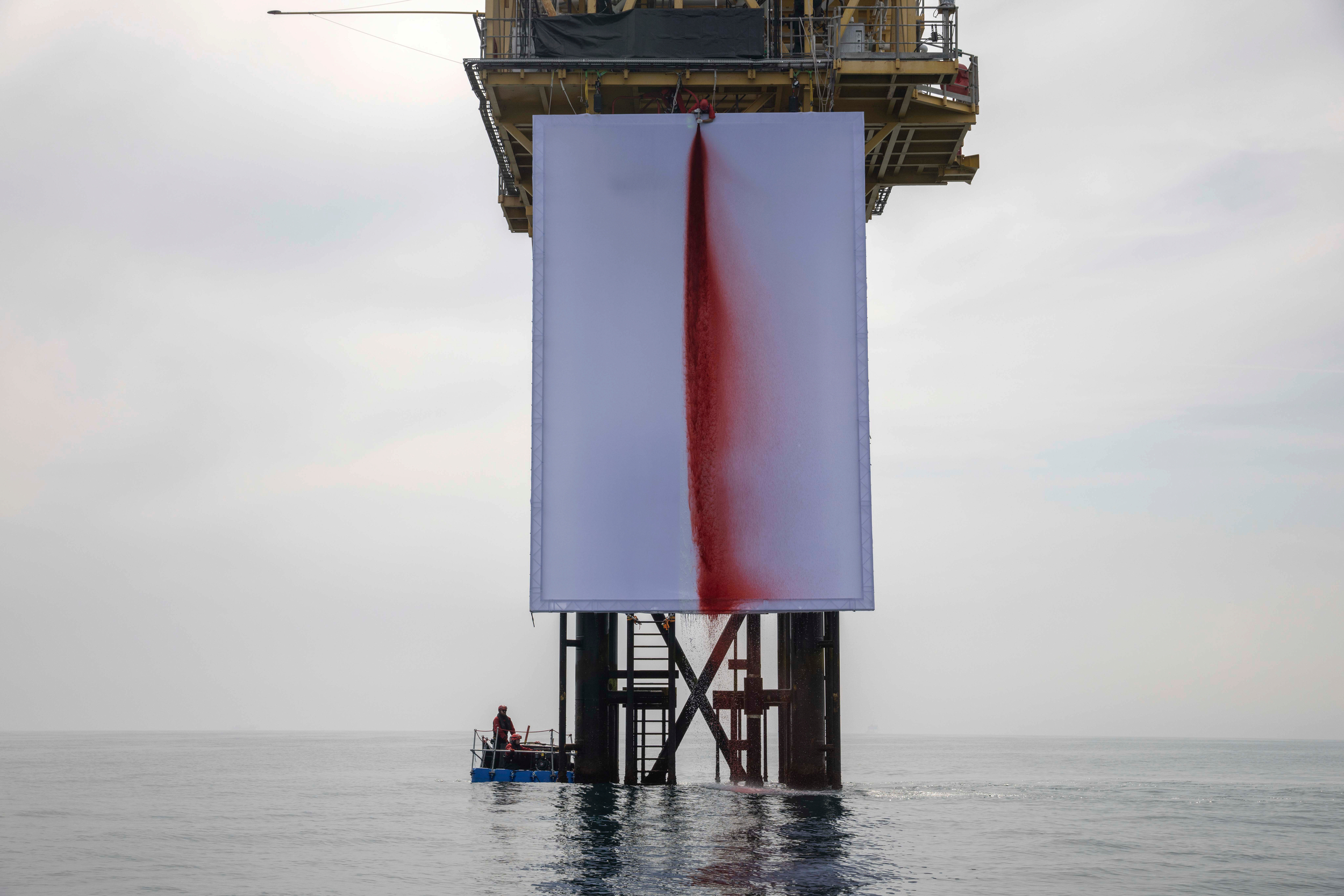 A view of a large white canvas with red paint down the middle on the lower structure of an oil platform