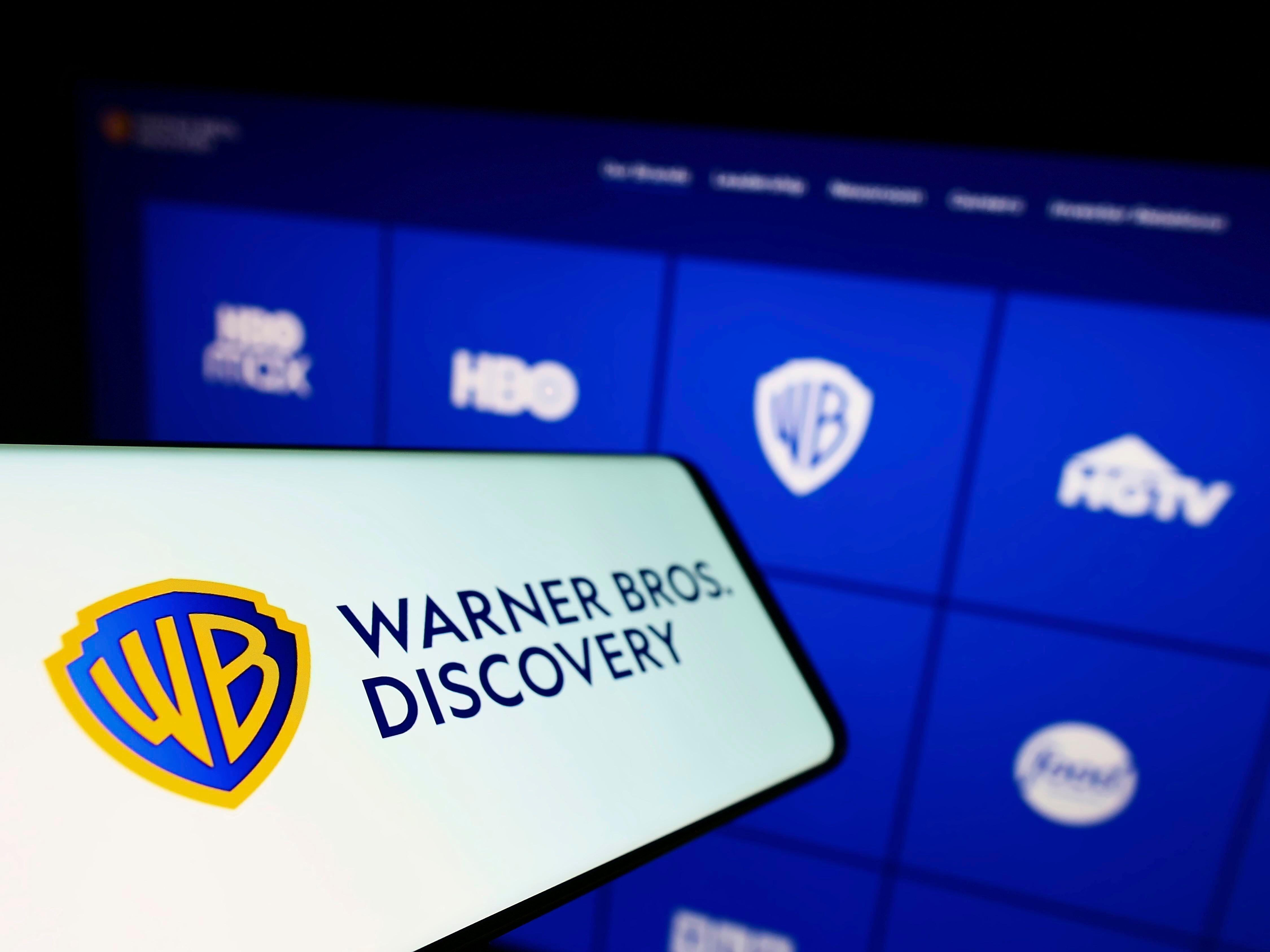A mobile phone with the logo of media company Warner Bros Discovery on screen in front of business website