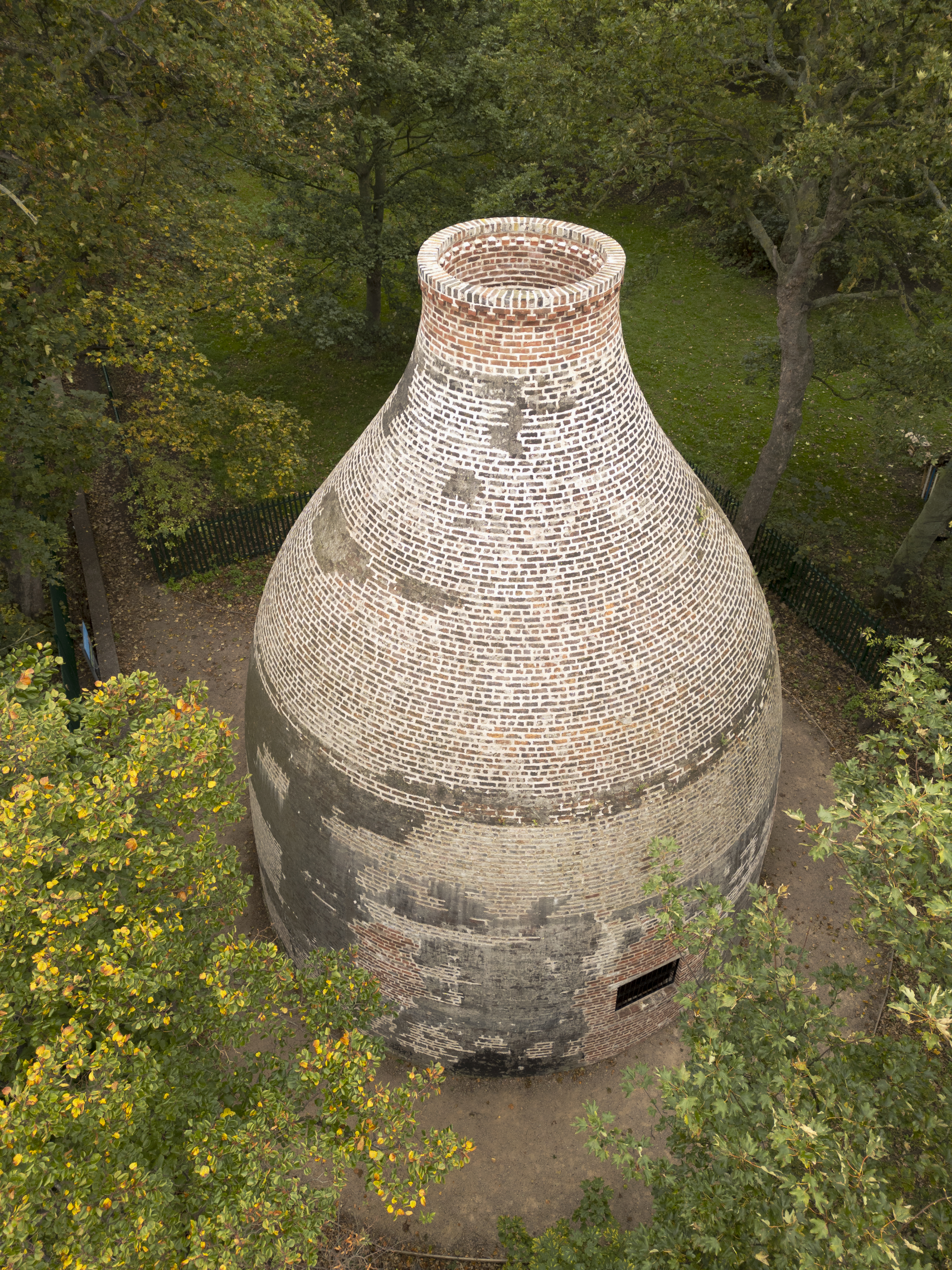 Aerial view of a large round brick kiln among trees, with repaired brick work at its tapered top