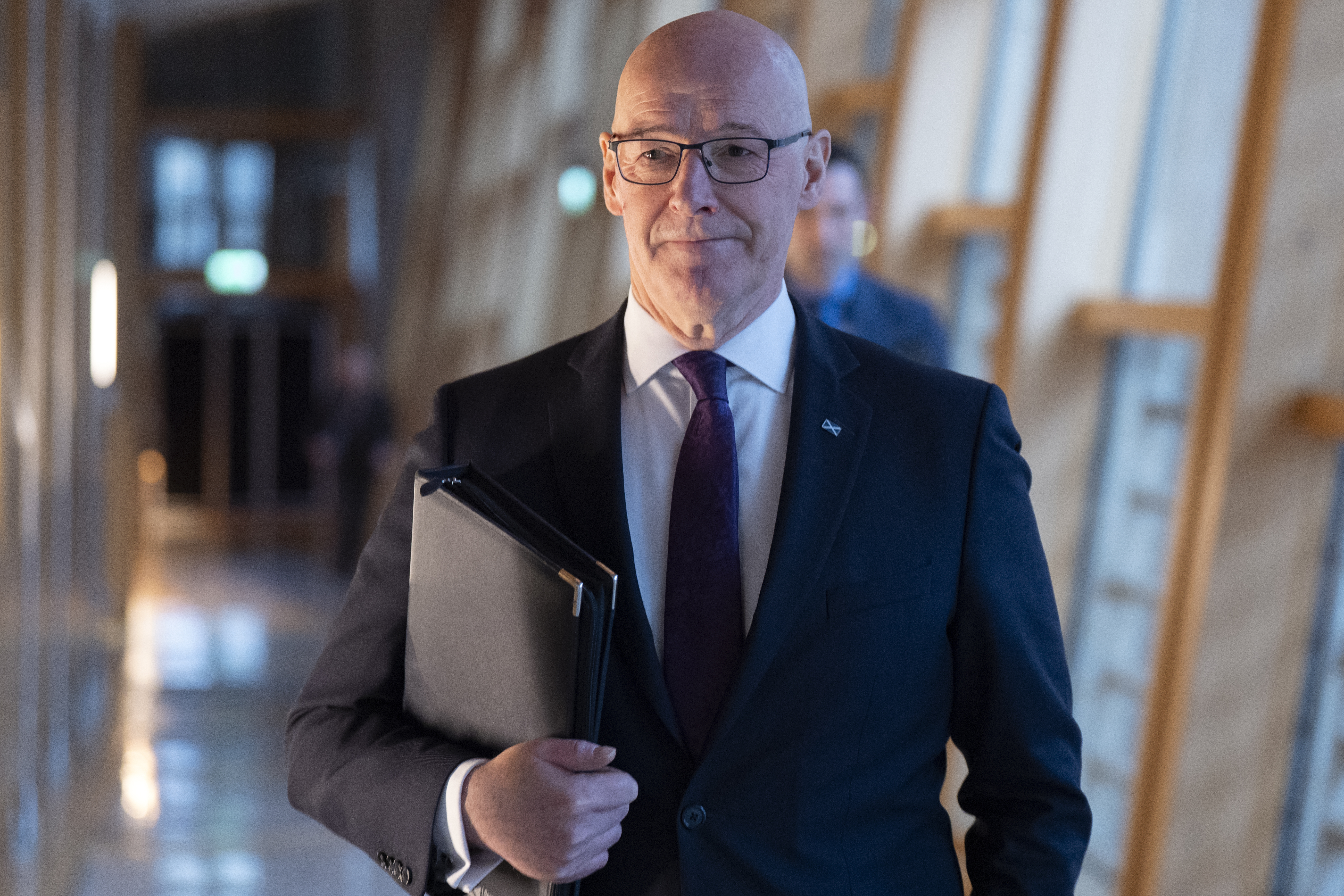 John Swinney walking through a corridor at Holyrood carrying a folder under his arm