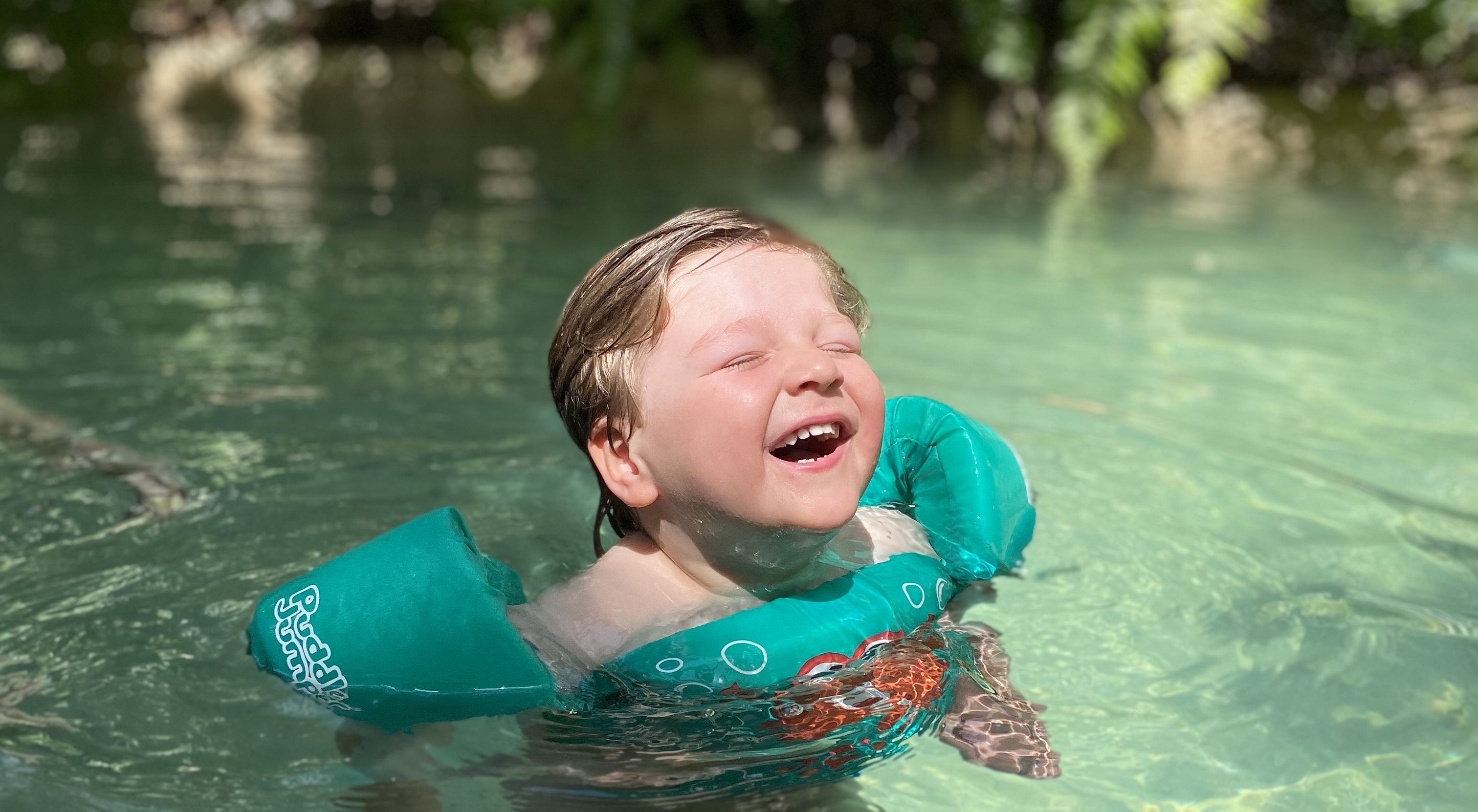 Three-year-old Nathaniel Clayton smiling with his eyes closed while swimming with armbands