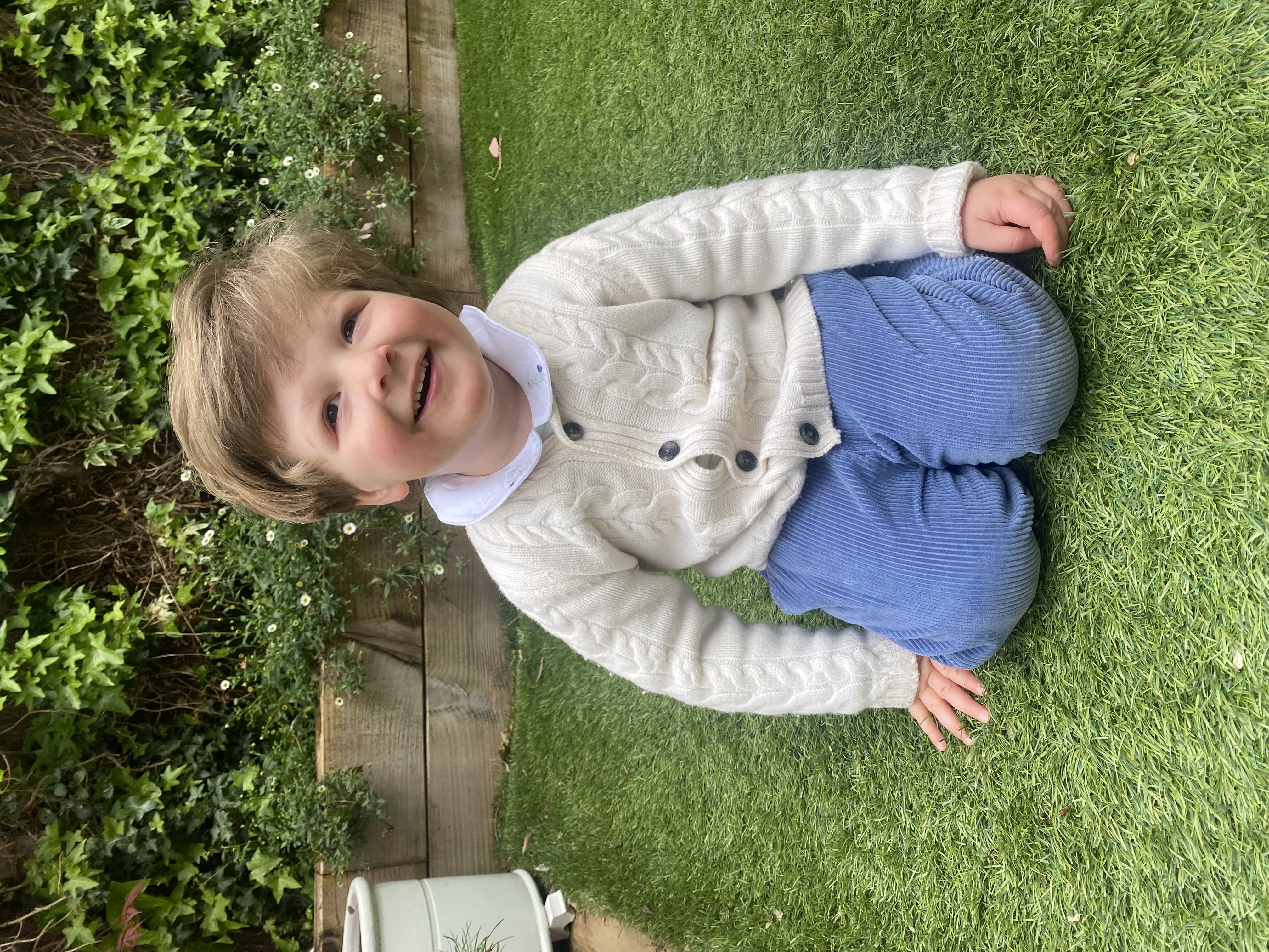 Three-year-old Nathaniel Clayton kneeling down on the grass smiling