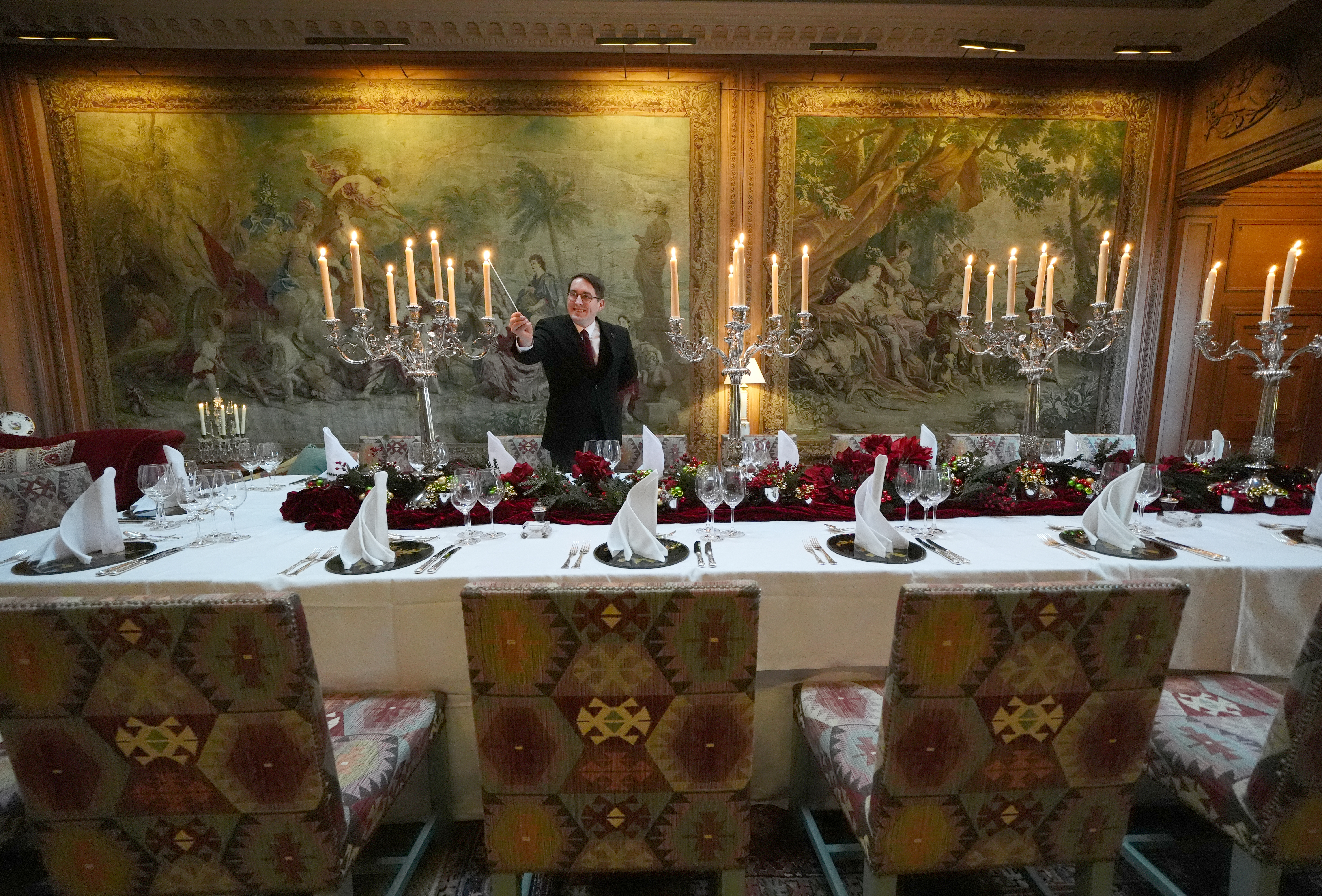 A man lights a candle on a large table set for a dinner service