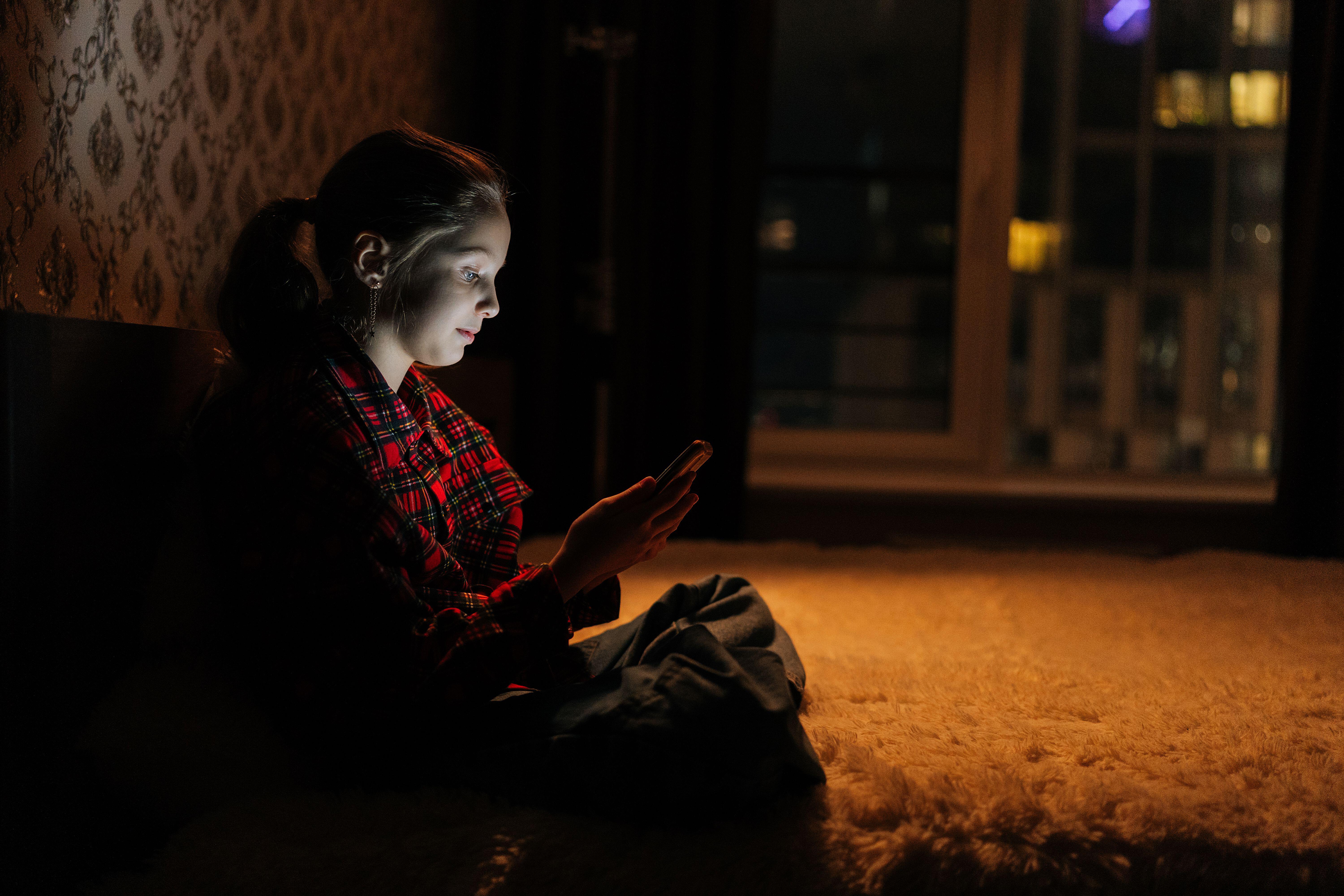 Side view of a young girl sitting on a bed in a dark bedroom