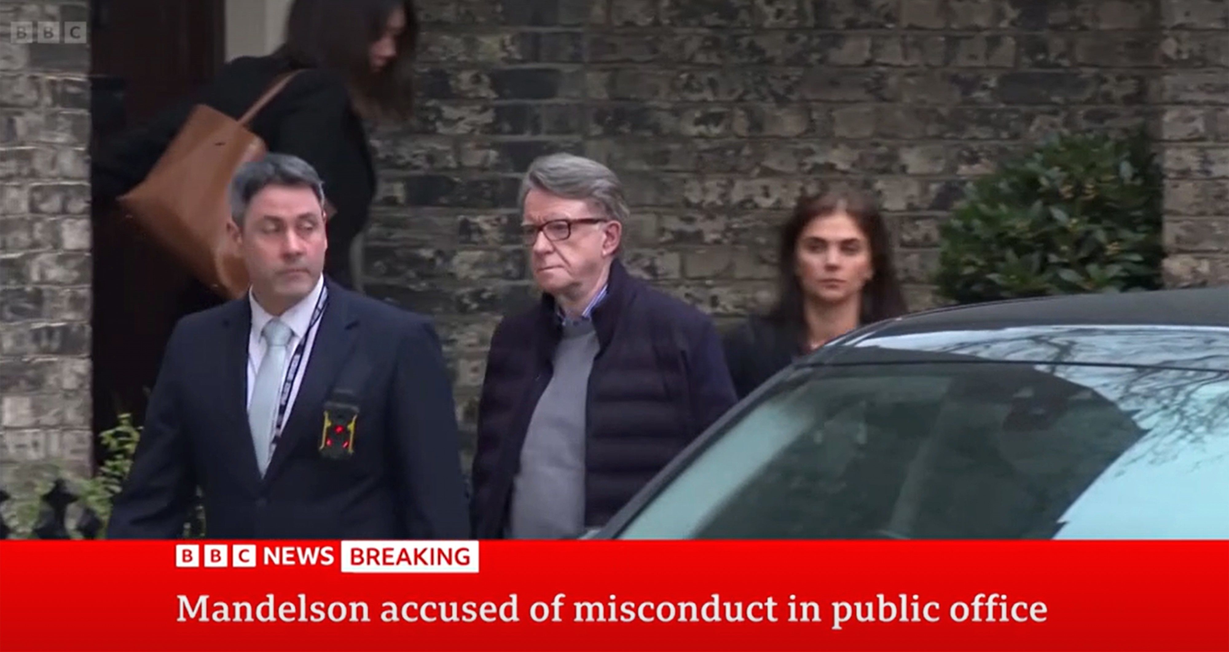 Screengrab of plain clothes police officer leading Lord Peter Mandelson out of a house in London