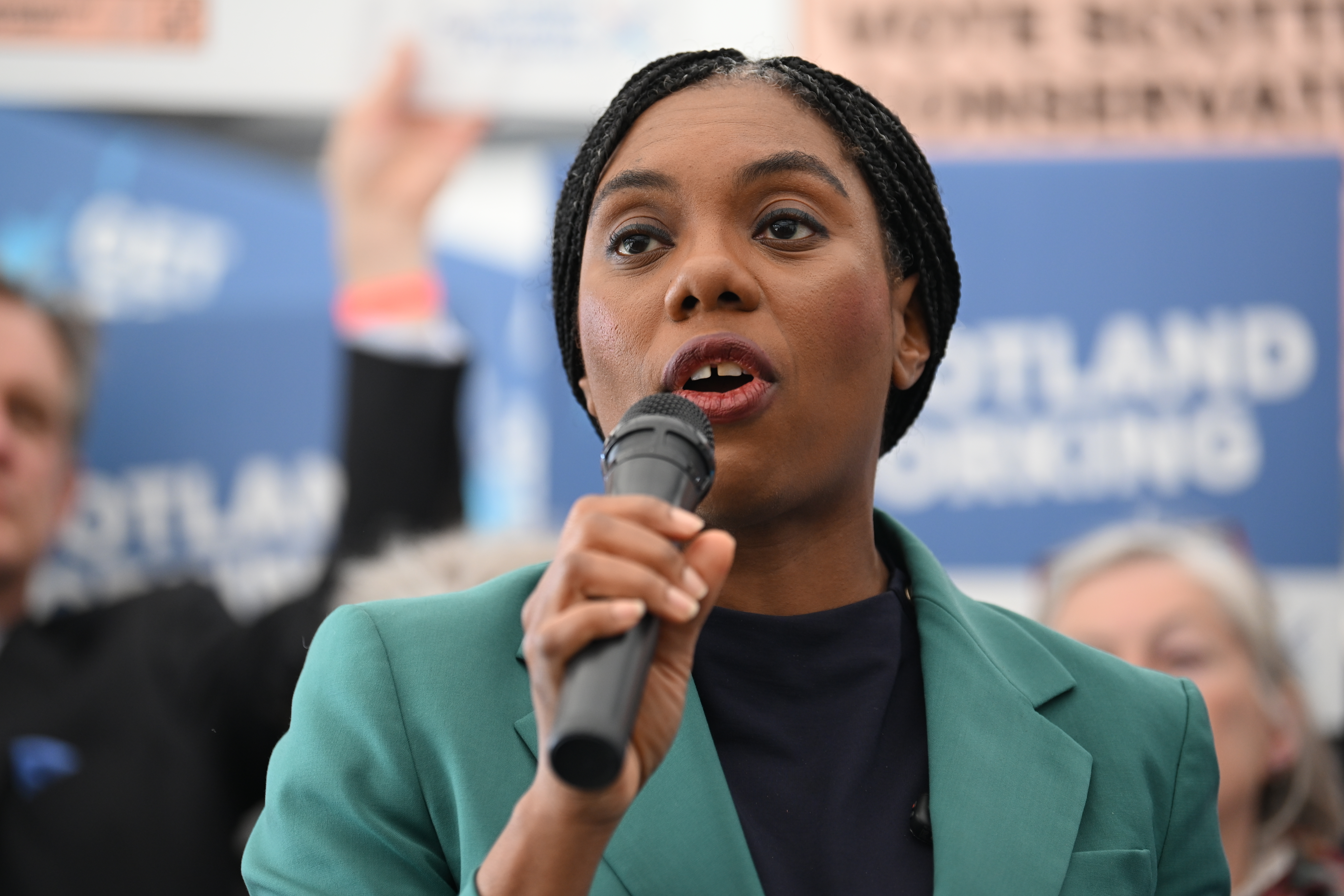 Kemi Badenoch speaking into a mic, in front of Tory supporters