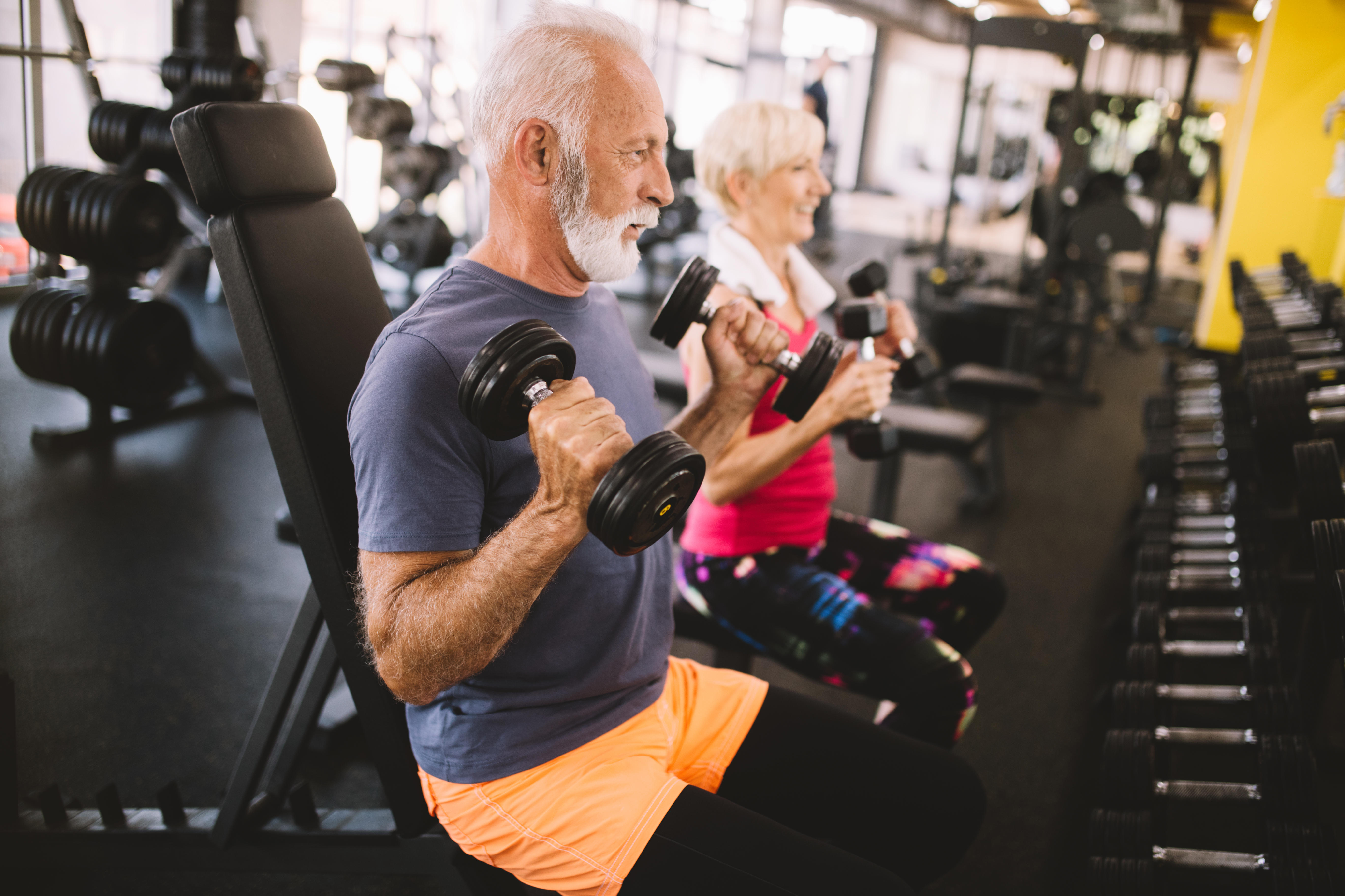 A senior man and woman lifting weights in a gym