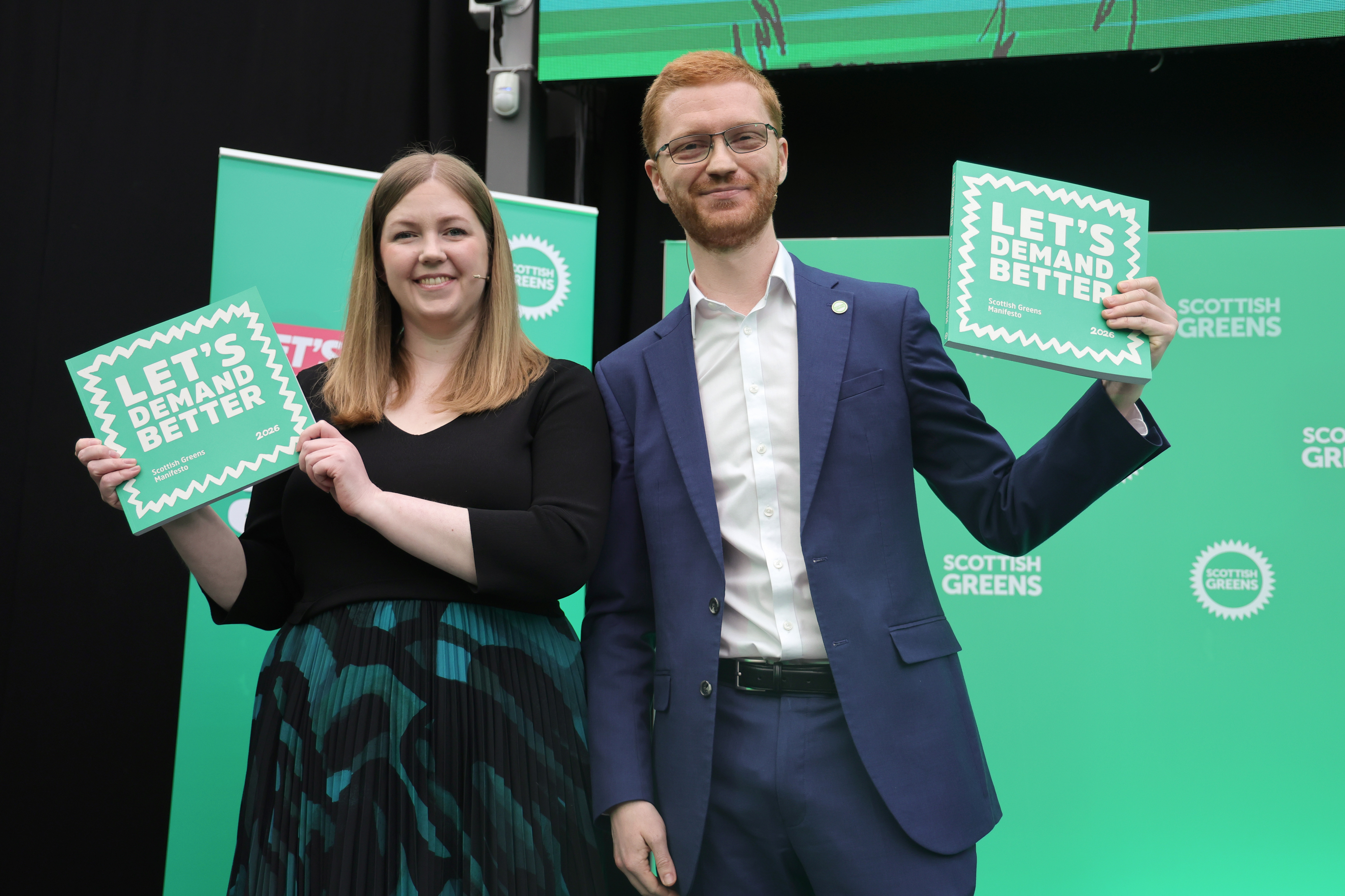 Gillian Mackay and Ross Greer smiling while holding up Scottish Green signage