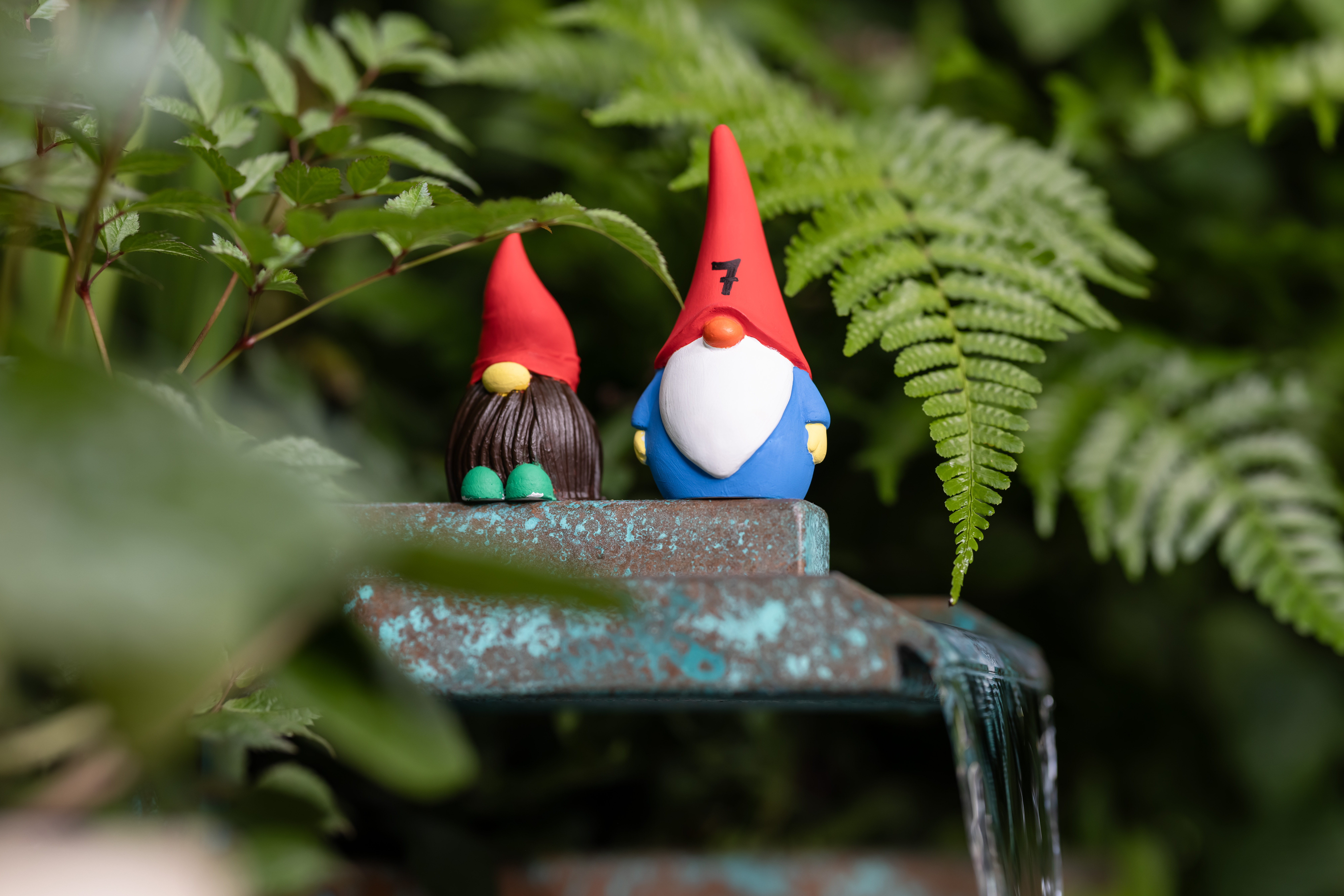 Two gnomes on a water feature, one with 7 on its red hat, and the other with long brown hair under a red hat