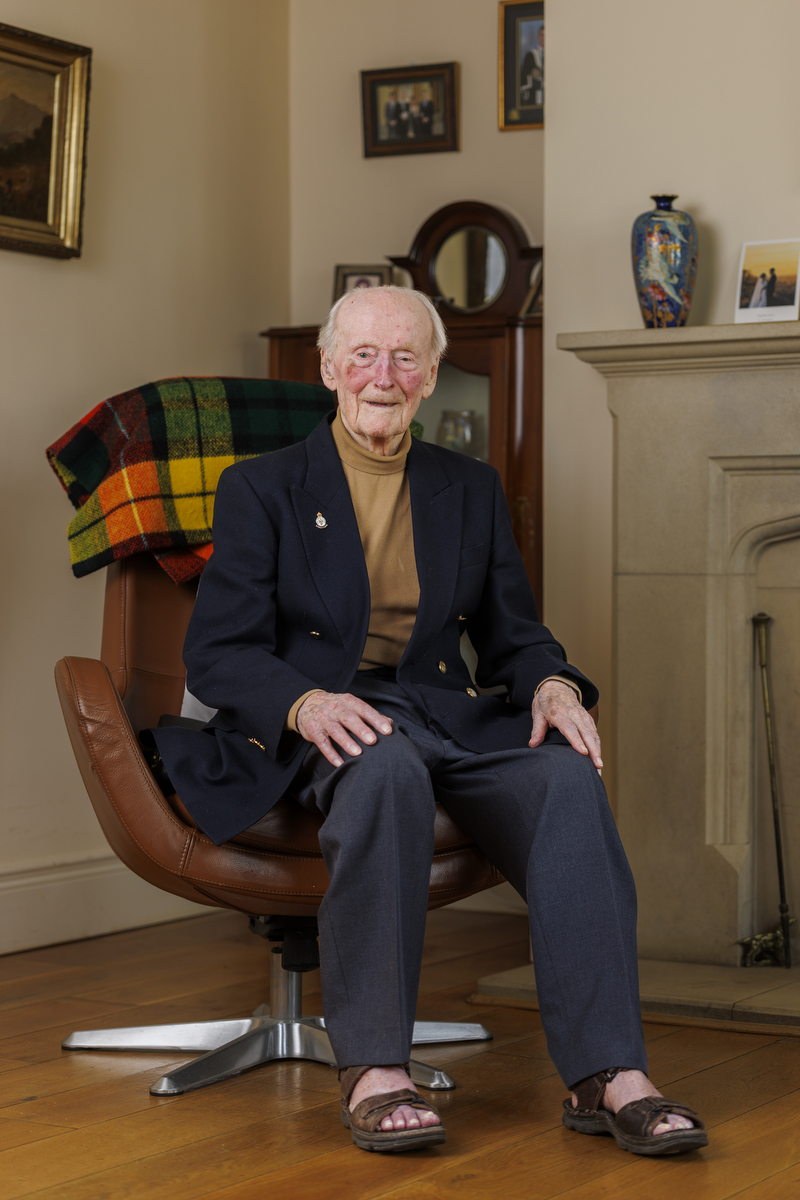 George Spencer smiling while seated in an armchair in a living room