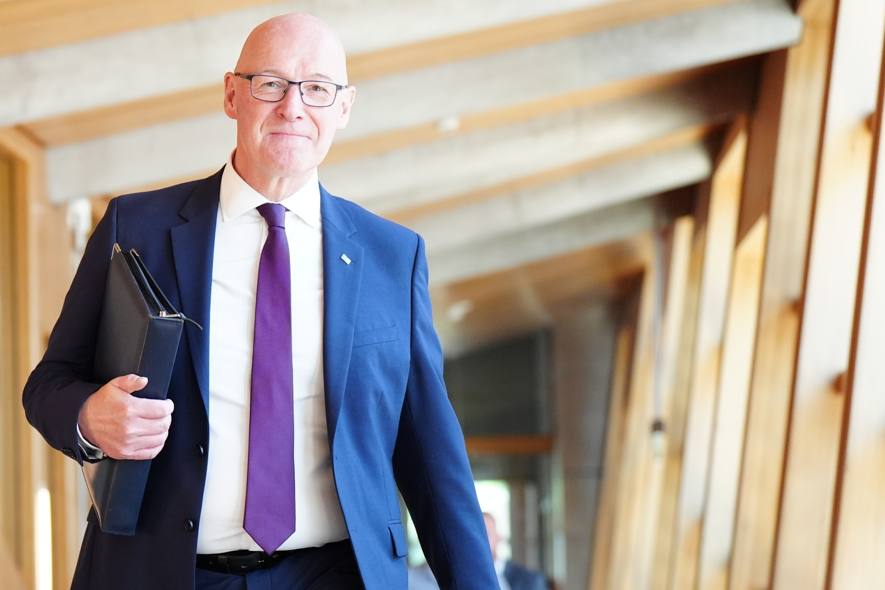 John Swinney holding a folder under his arm while walking inside the Scottish Parliament