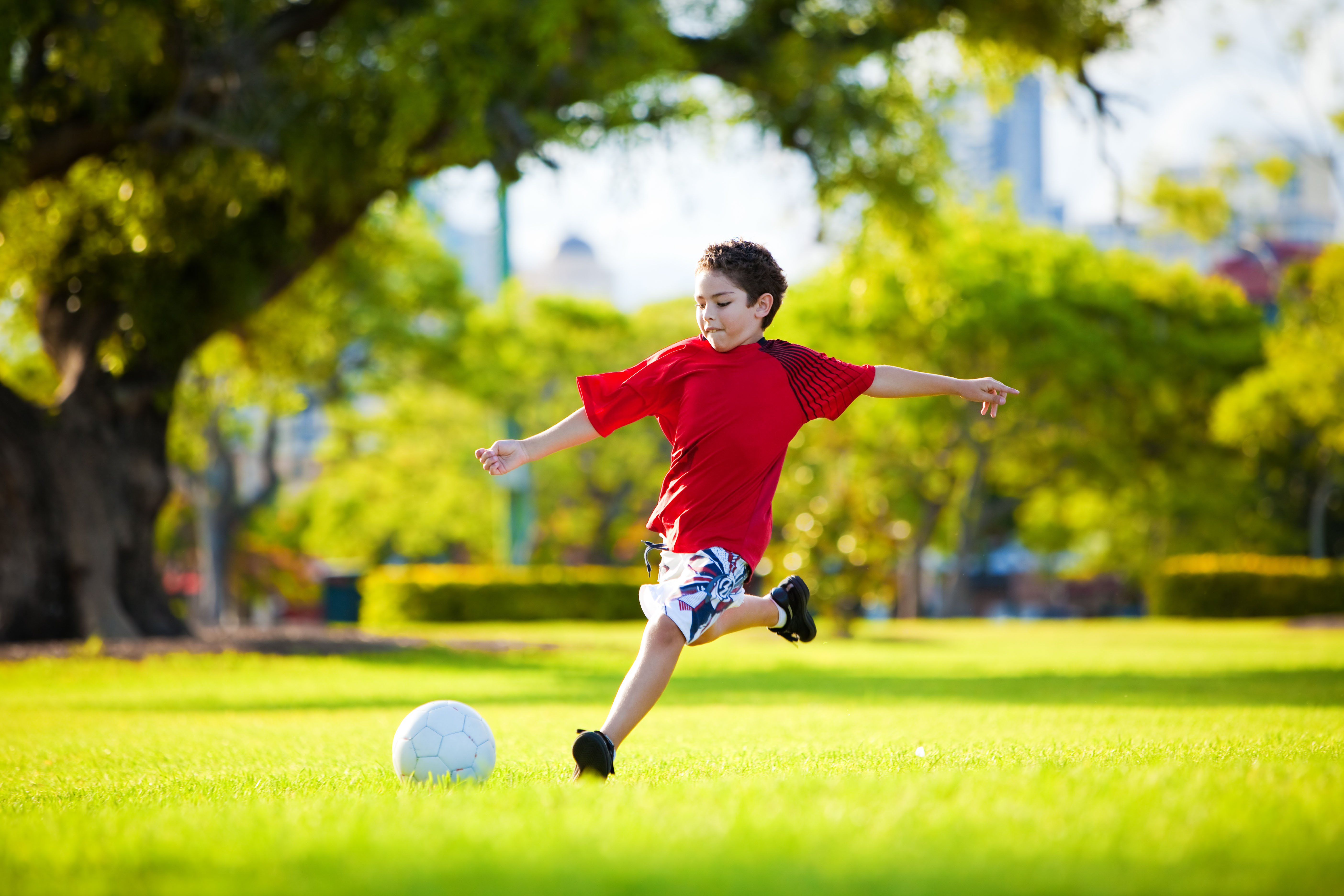 Young excited boy kicking ball in the grass outdoors