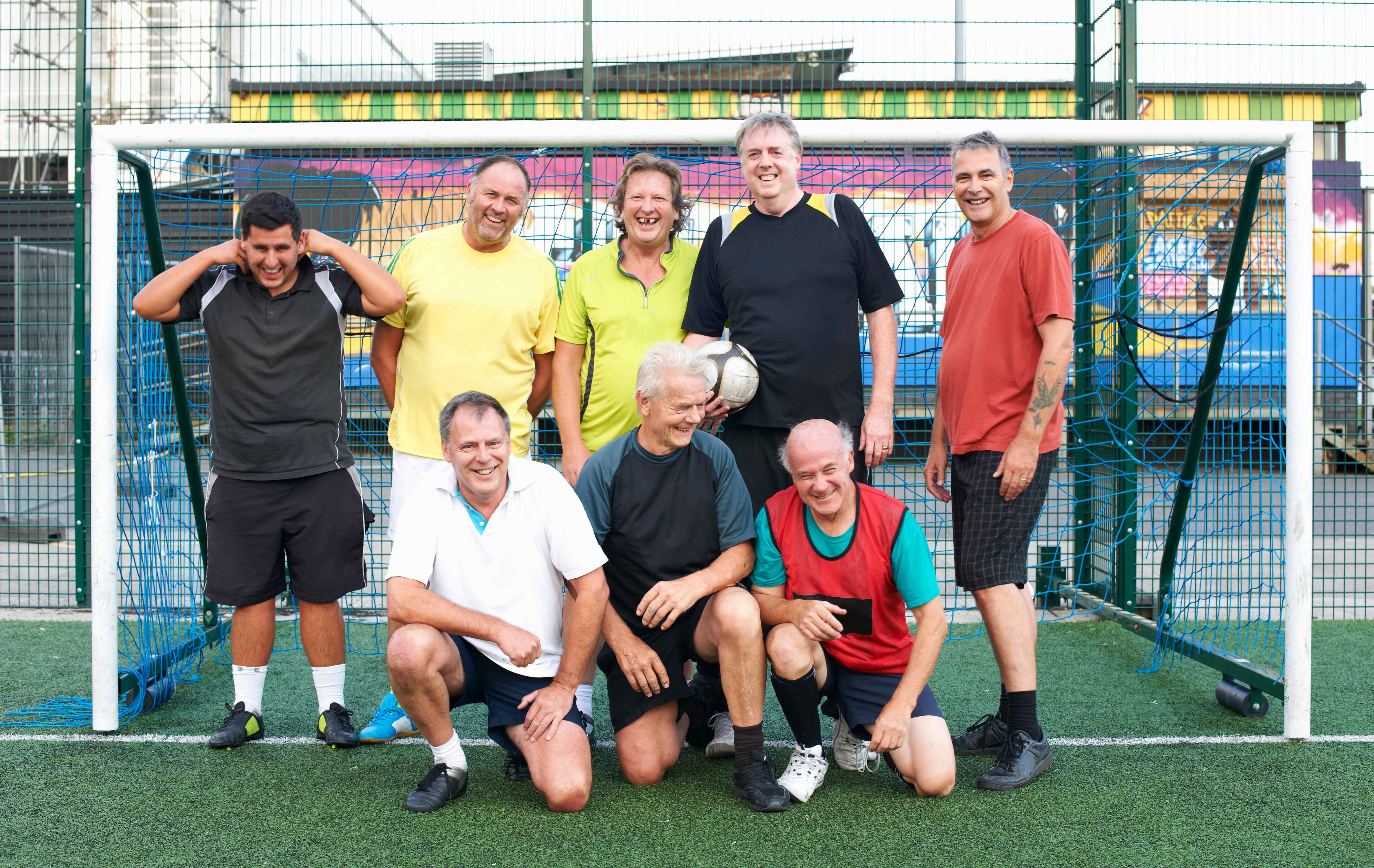 Group of older men smiling on a football pitch next to a goal