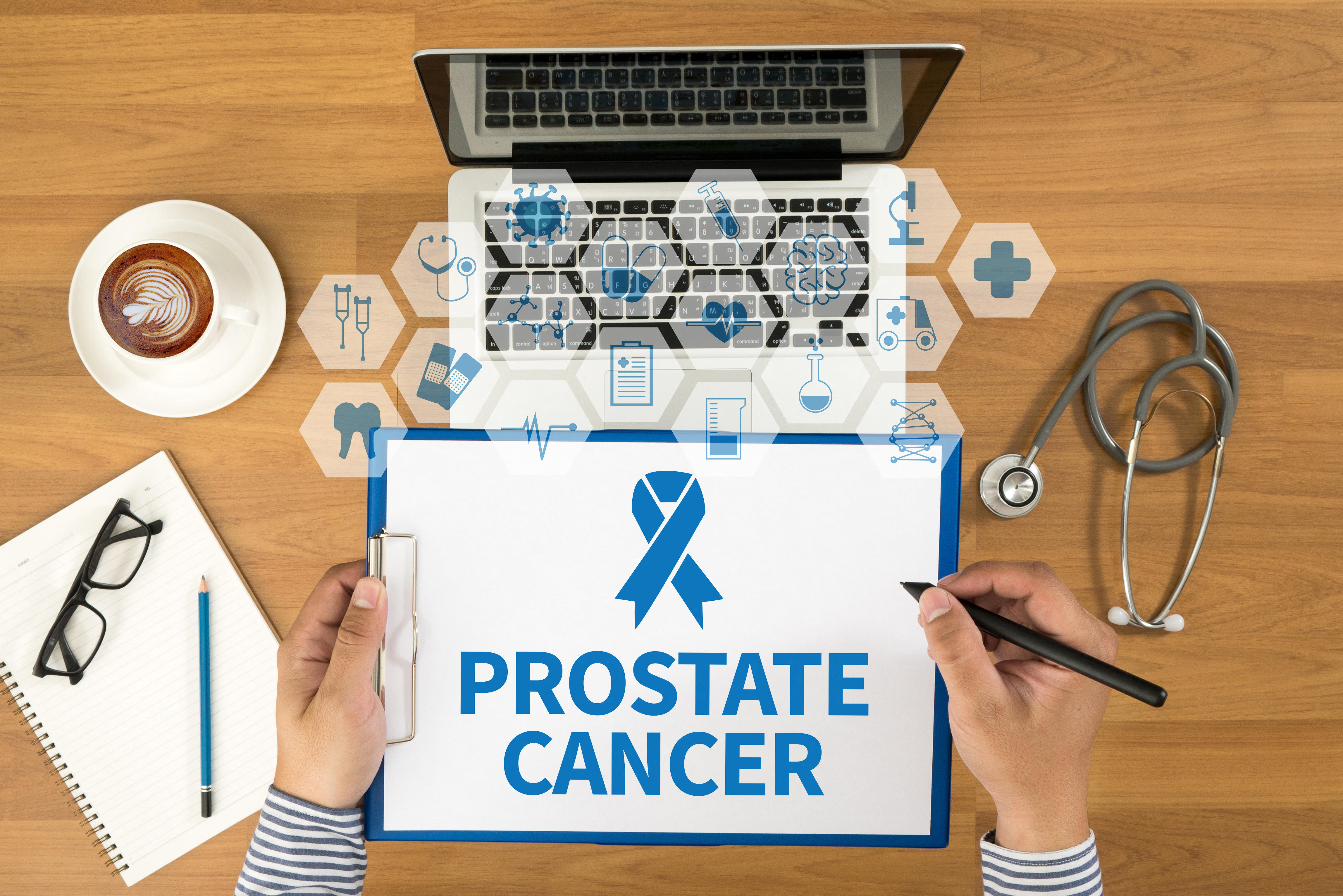 Doctor looking at a laptop and medical notes which have prostate cancer and a blue ribbon printed on it