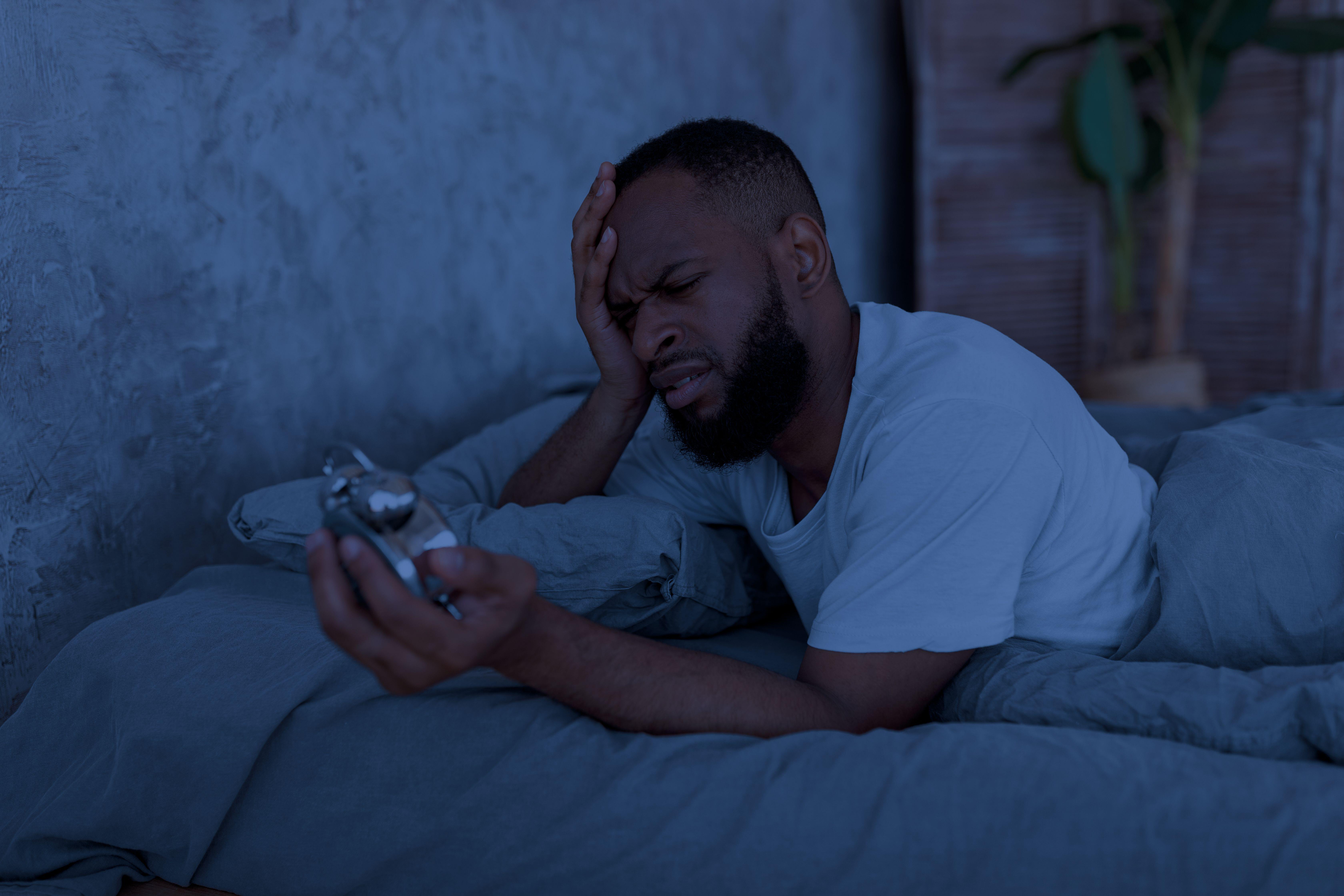 Man suffering from insomnia looking at clock