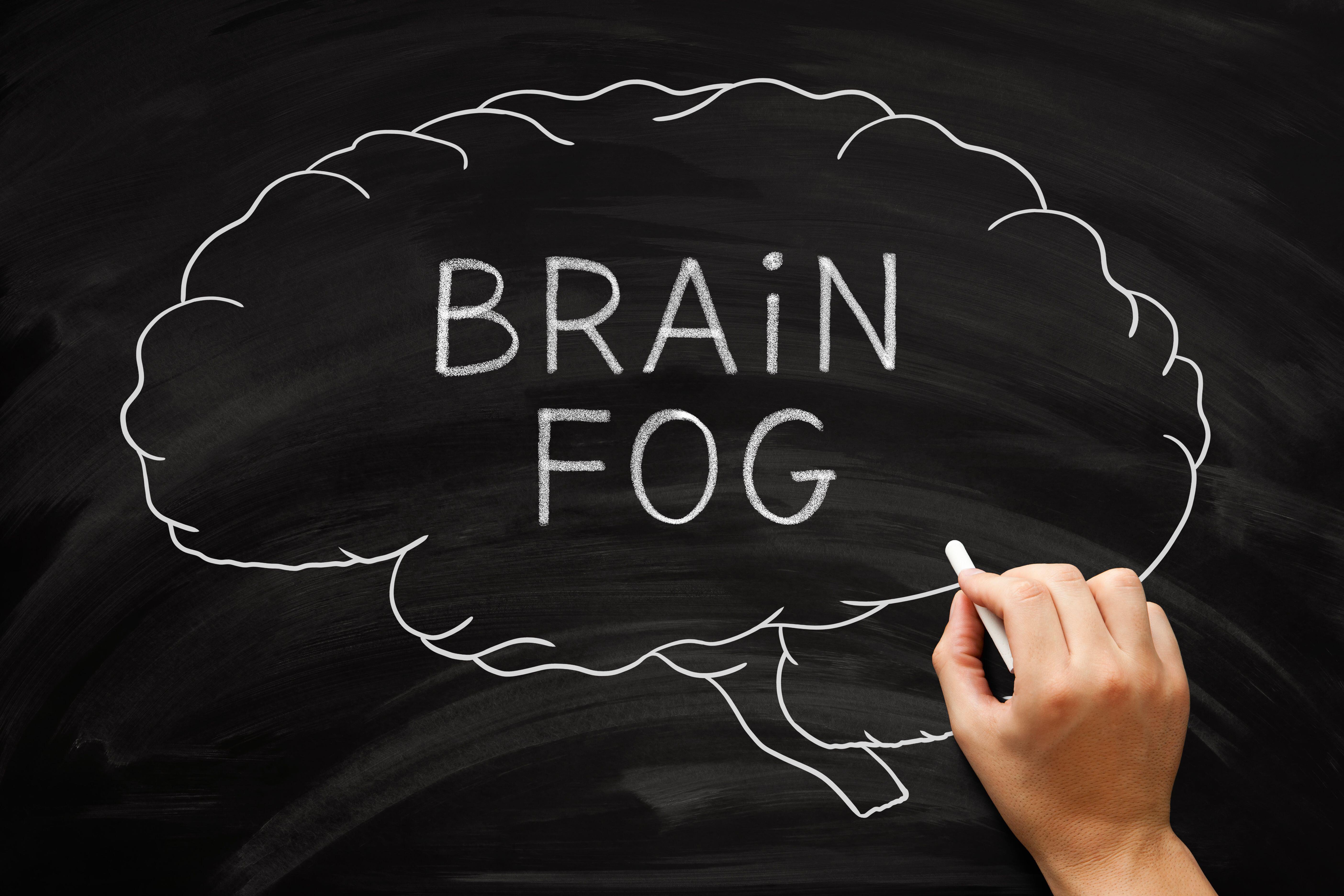 Hand drawing a chalk outline of a brain with the words brain fog written inside it