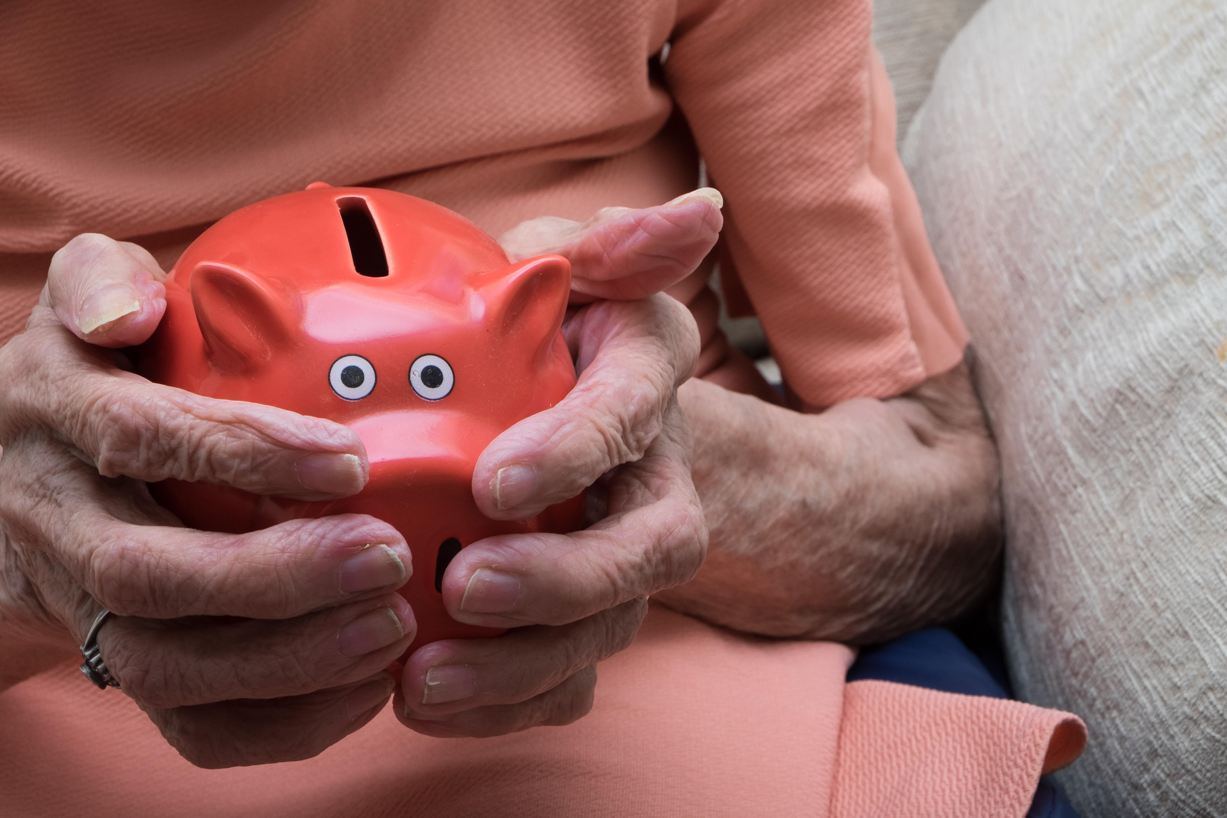 The hands of an elderly woman holding a piggy bank