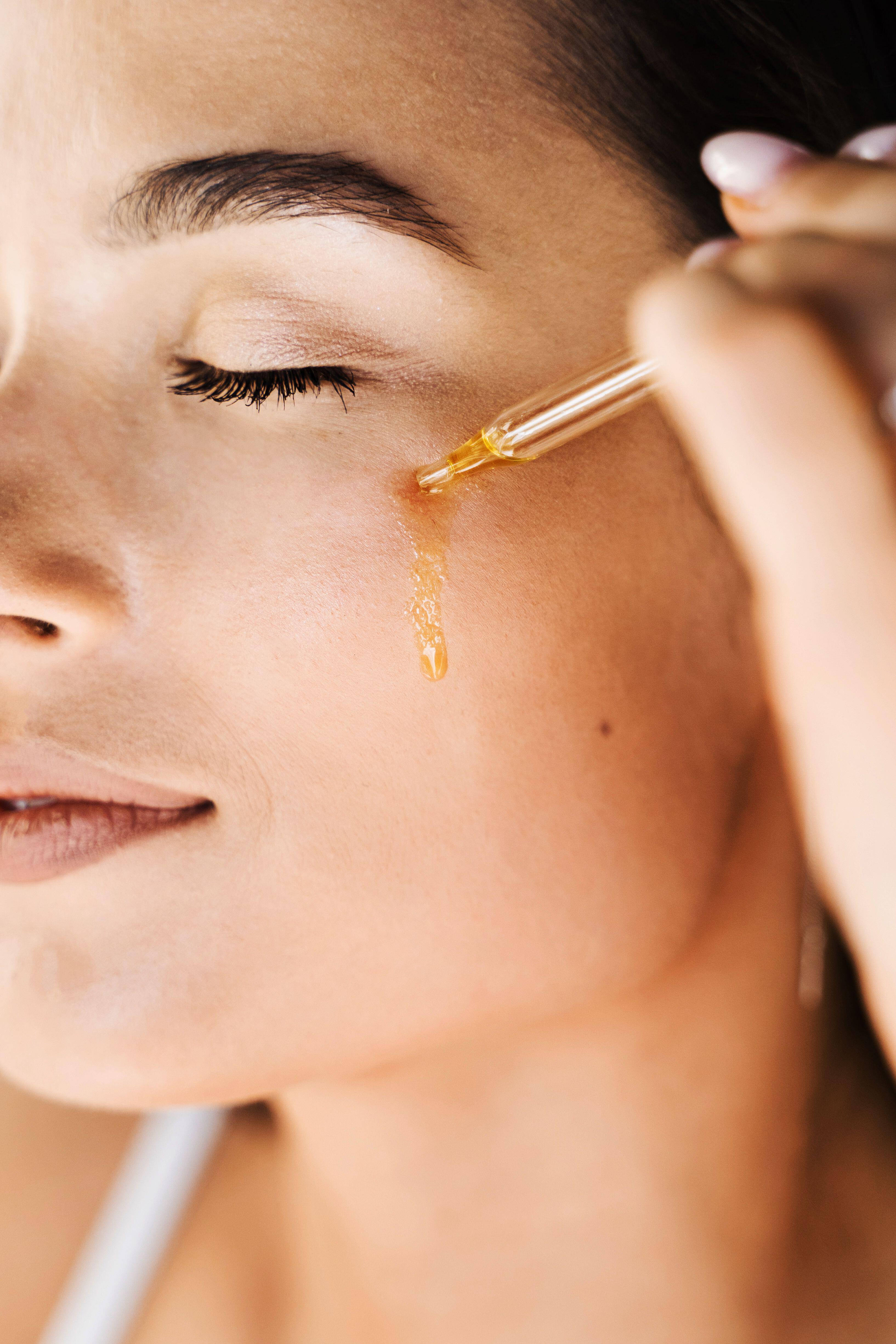 Attractive girl drops essential oil on facial skin close-up. Young woman is applying moisturizing serum on her face