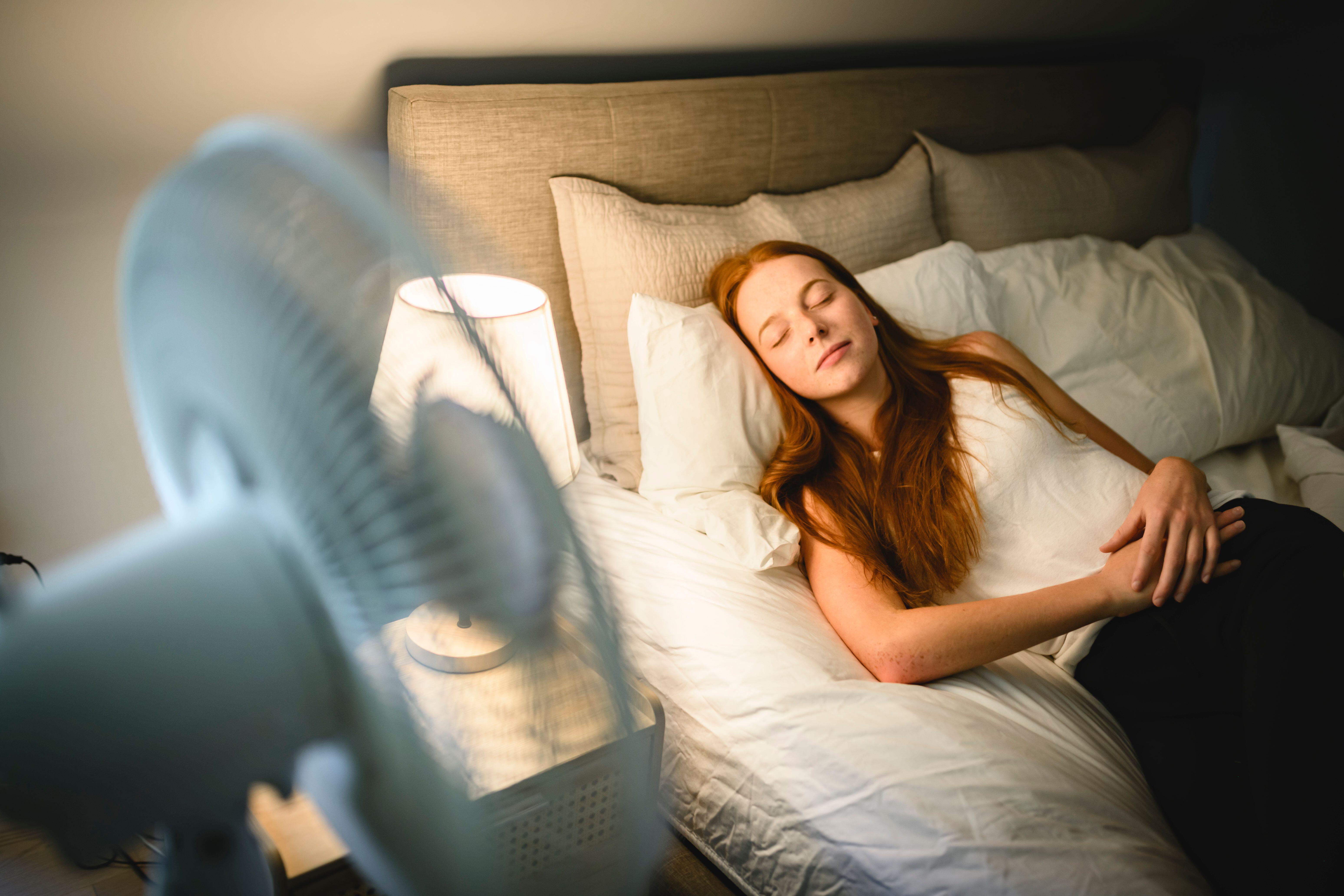 Young woman with red hair sleeping in bed peacefully next to a fan