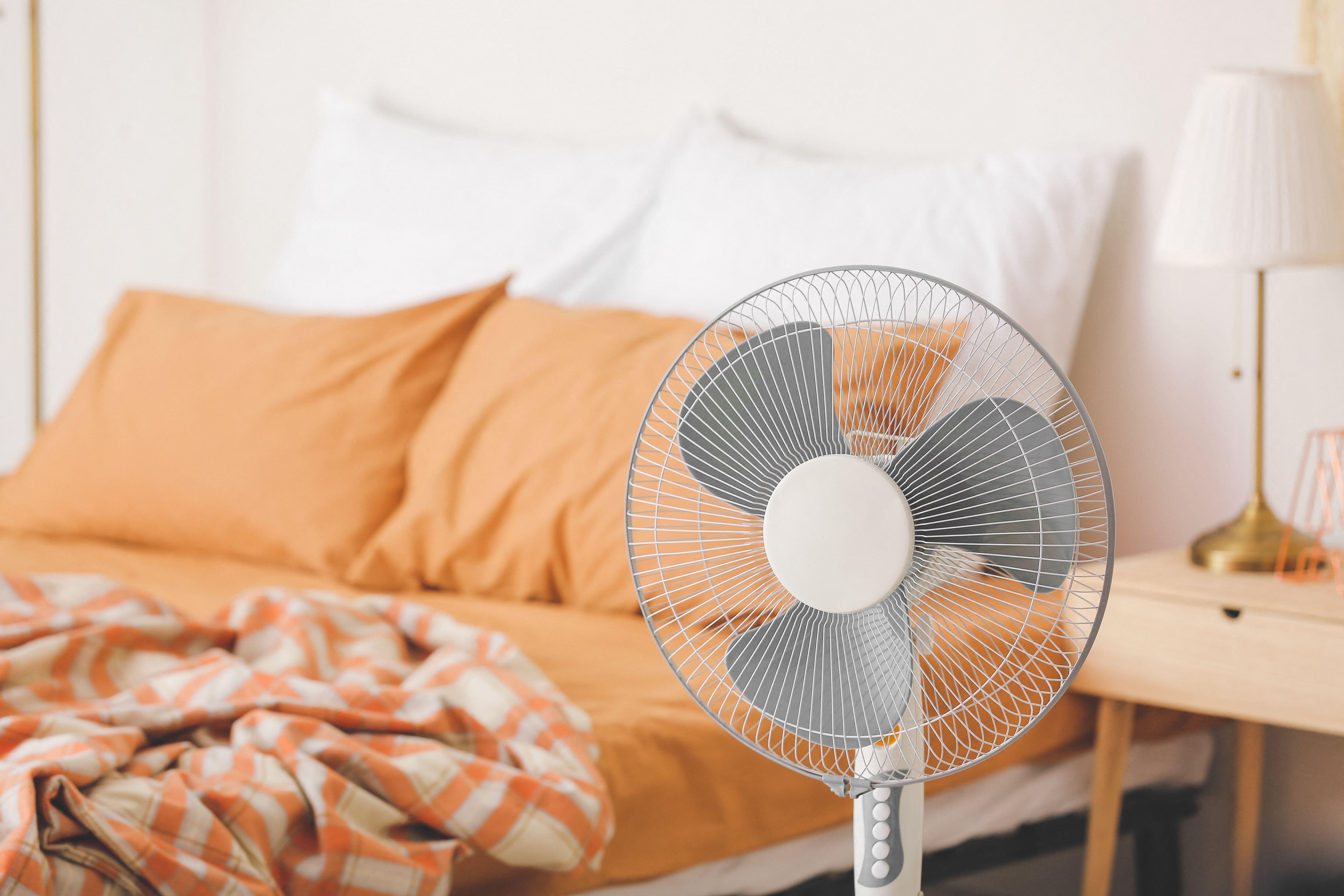 Modern electric fan in bedroom pointed away from orange themed bed