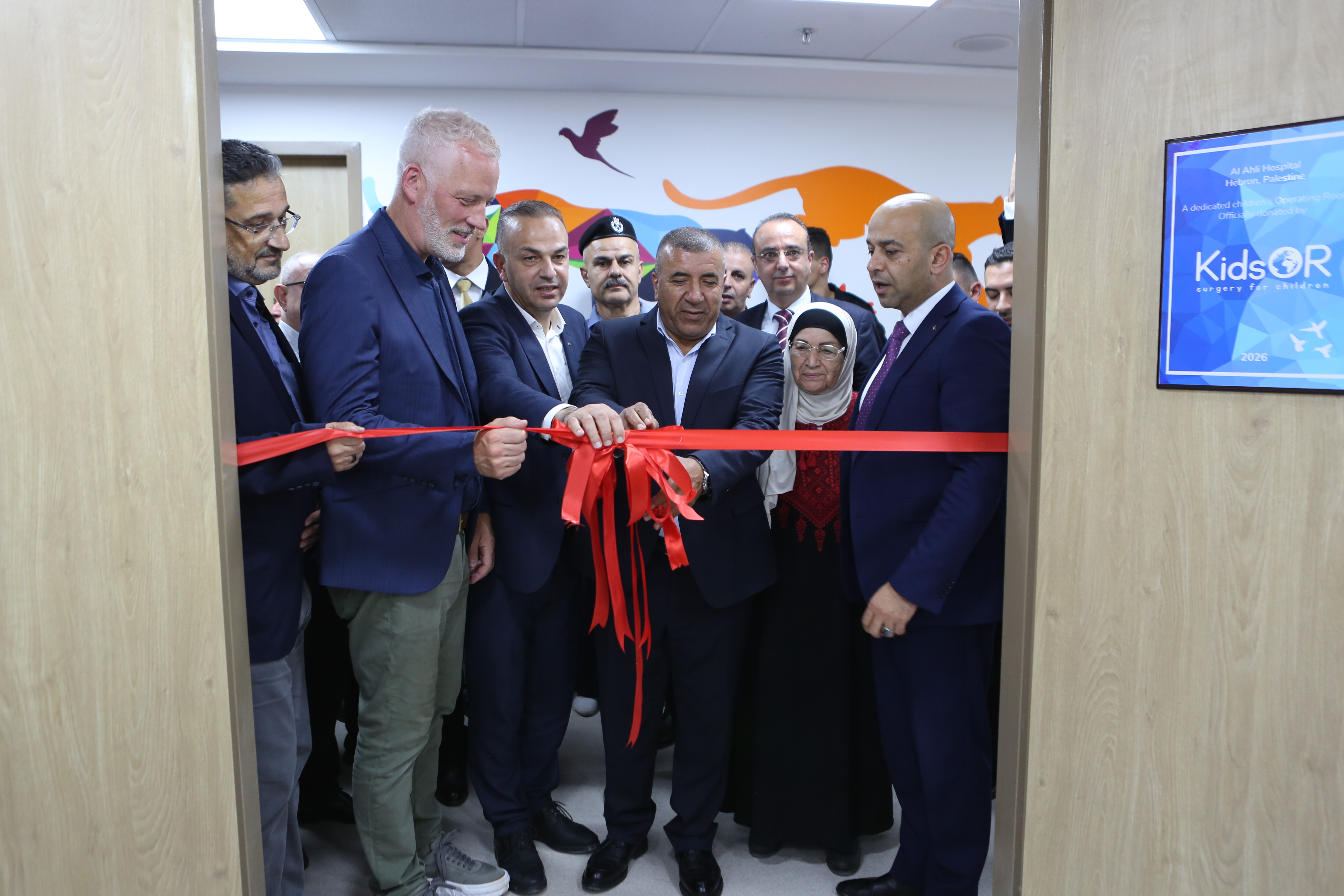 A group of people watch as a large red ribbon is cut