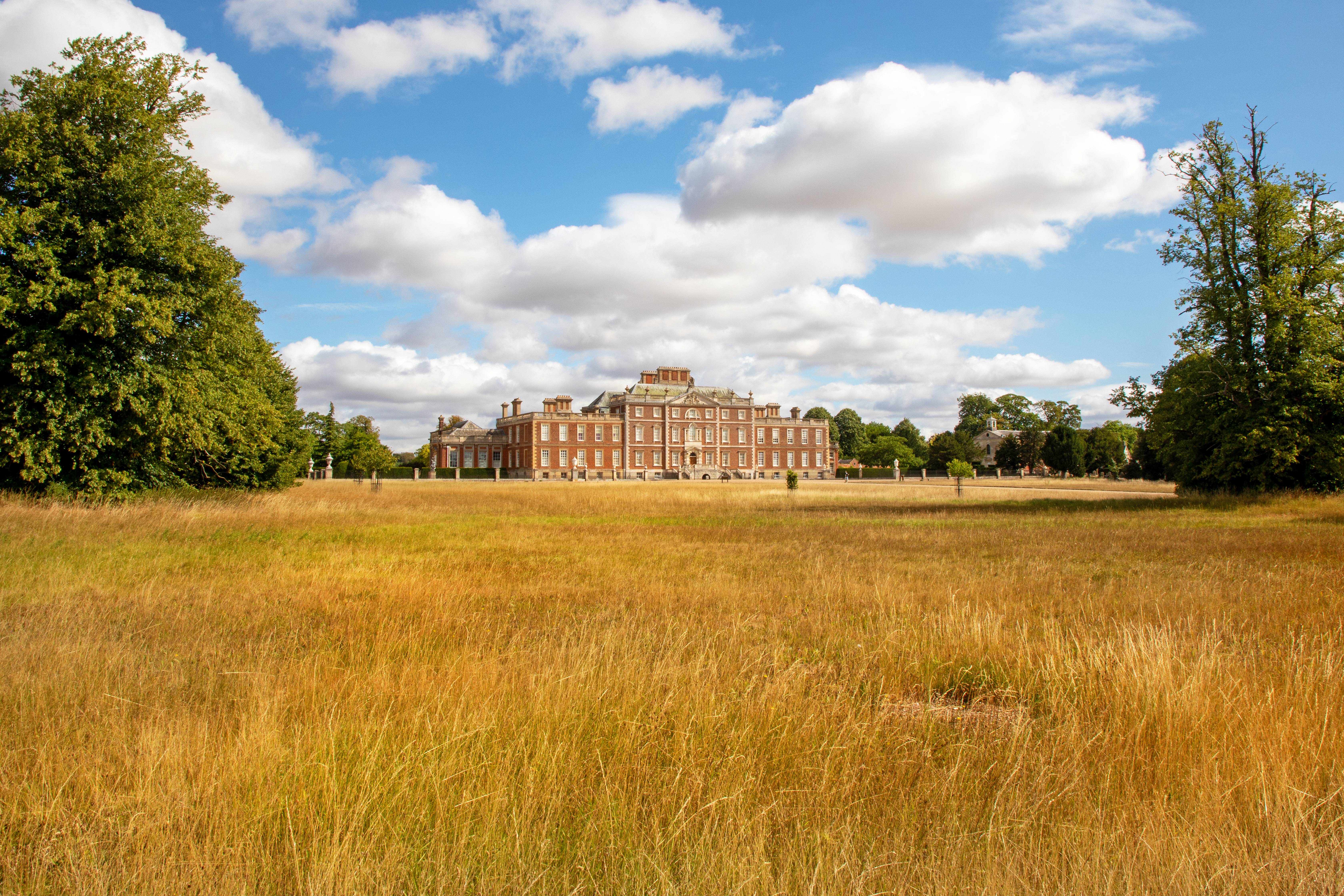 A view of a large manor house, with dry, brown grass in the foreground