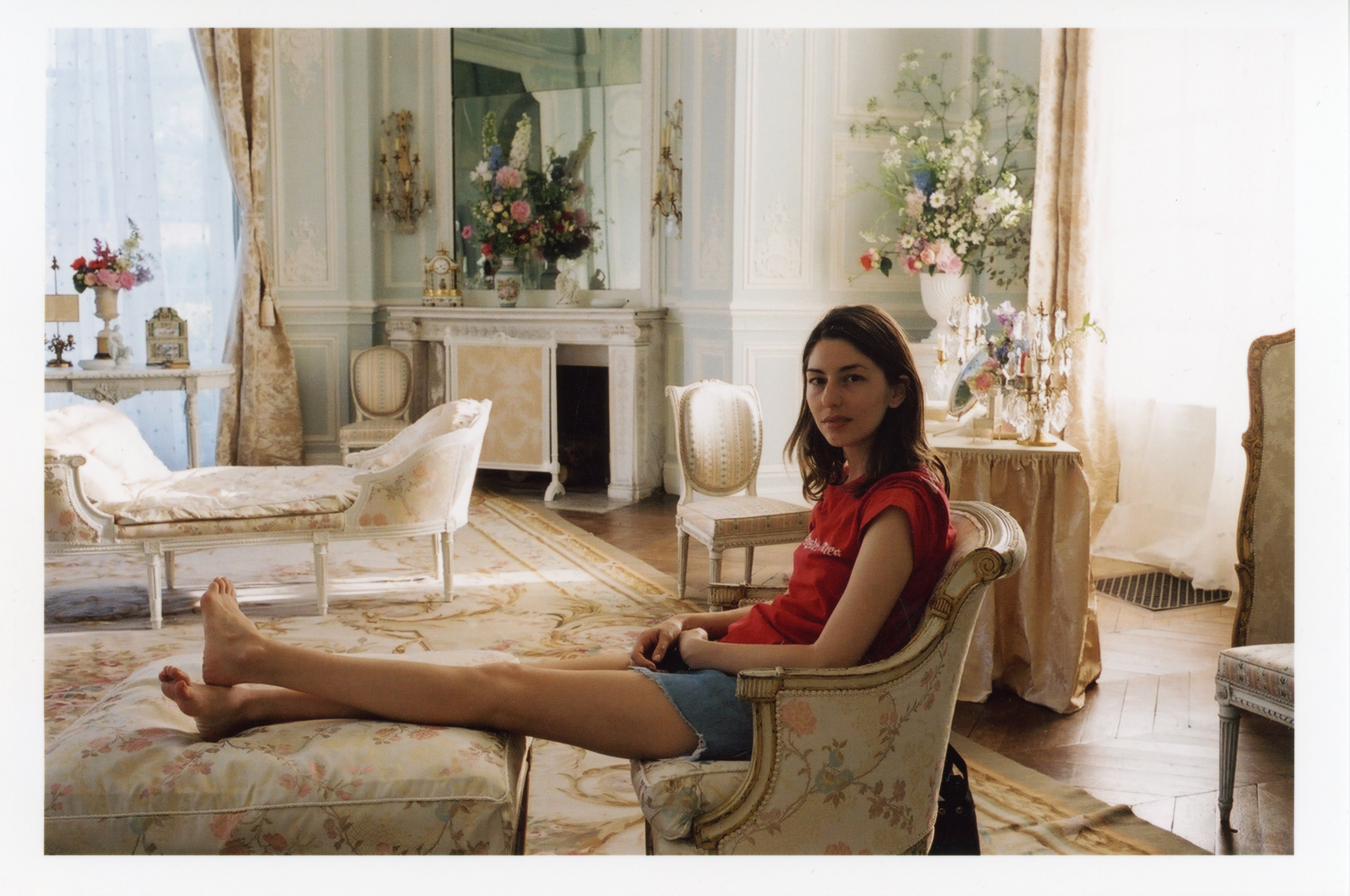 Sofia Coppola seated, with her legs on a foot rest, on set