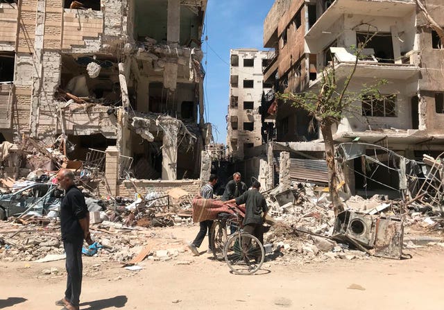People stand in front of damaged buildings, in the town of Douma in April 2018