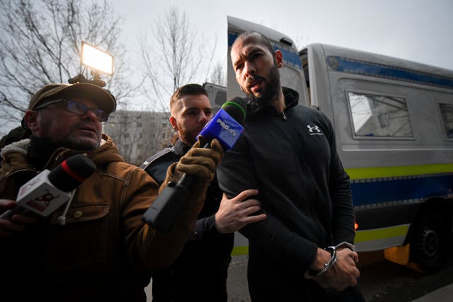 Police officers escort Andrew Tate to the offices of the Directorate for Investigating Organized Crime and Terrorism (Diicot), where prosecutors are examining his electronic equipment