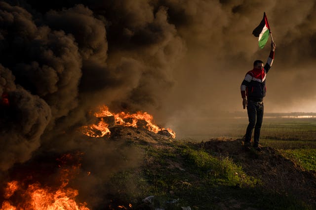 Palestinians burn tyres and wave the national flag during a protest against a Israeli military raid in the West Bank city of Jenin, along the border fence with Israel, east of Gaza City