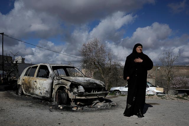 A Palestinian woman stands next to a burnt car in the village of Jalud near the West Bank town of Nablus