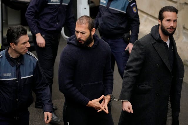 Police officers escort Andrew Tate, centre, handcuffed to his brother Tristan Tate, to the Court of Appeal in Bucharest