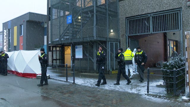 Police officers stand in front of a building used by Jehovah’s Witnesses in Hamburg after a shooting left eight people dead