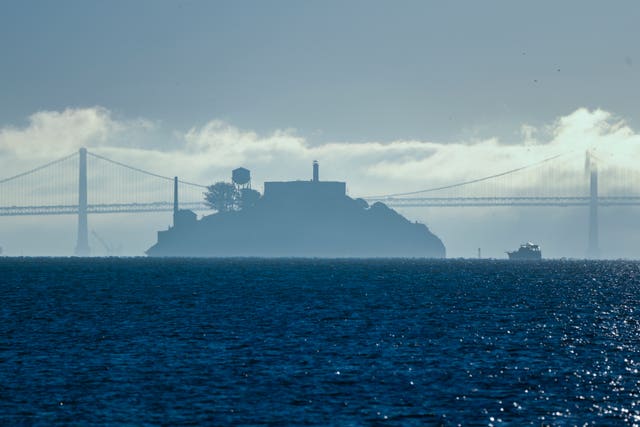 A boat makes its way toward Alcatraz Island with the San Francisco-Oakland Bay Bridge in the background
