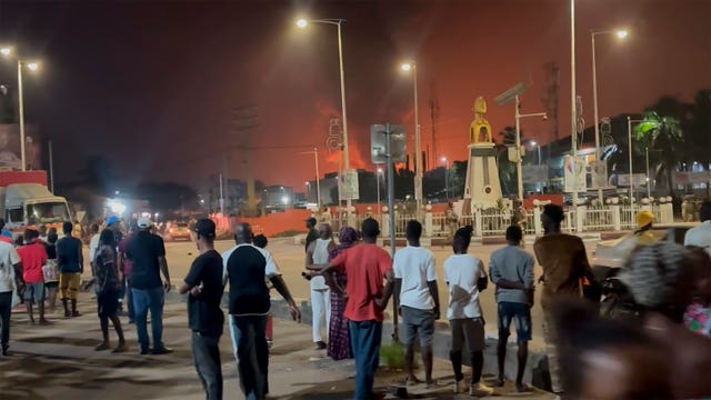 Residents watch a plume of smoke from a burning oil depot in Conakry, Guinea, on Monday