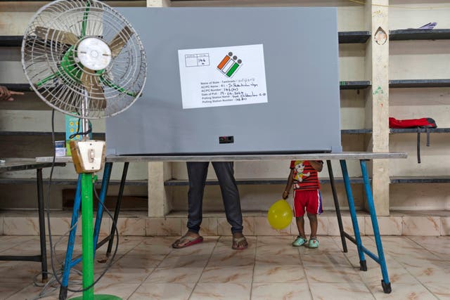 A child holding a balloon stands next to an adult casting his vote at a polling station in southern Tamil Nadu state 