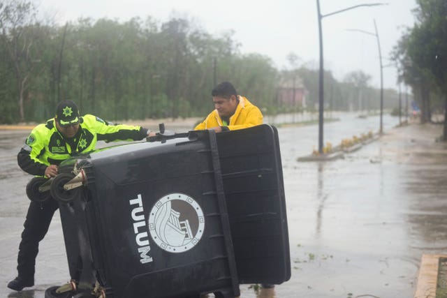 A police officer helps to upright a toppled trash bin in the aftermath of Hurricane Beryl in Tulum, Mexico