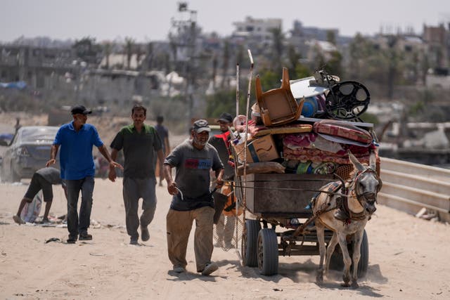 A cart pulled by a donkey piled high with belongings. A man walks alongside it