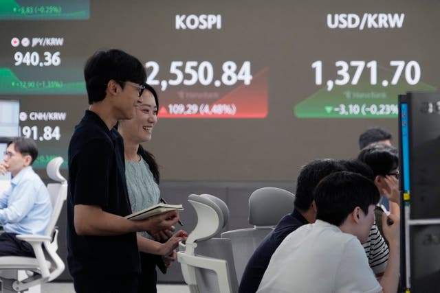 Currency traders watch monitors near a screen, back, showing the Korea Composite Stock Price Index in Seoul