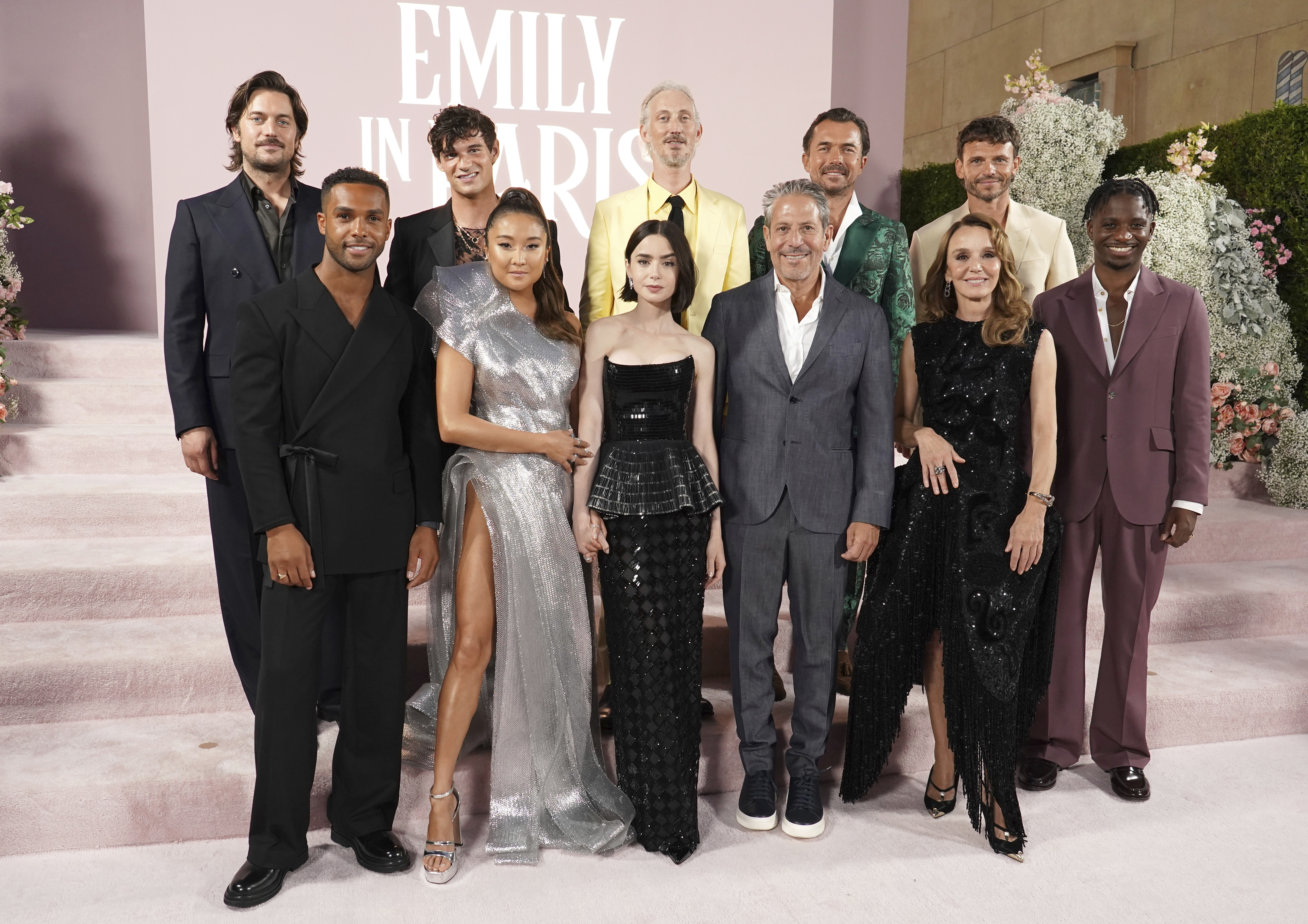 The cast of Emily in Paris smile together on lilac carpet
