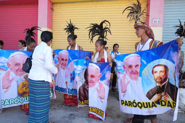 People with traditional dress hold banners of Pope Francis as they prepare to welcome the pope’s visit