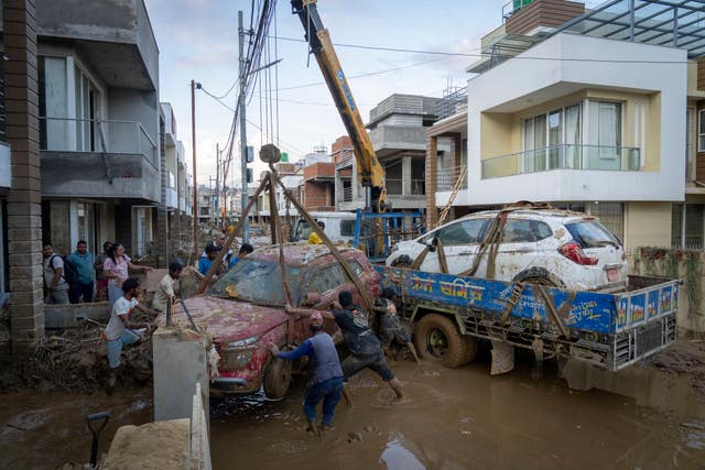 A group of men use a crane to lift a car off a muddy street