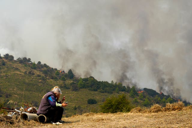 People sit as flames burn a forest in Sofiana village