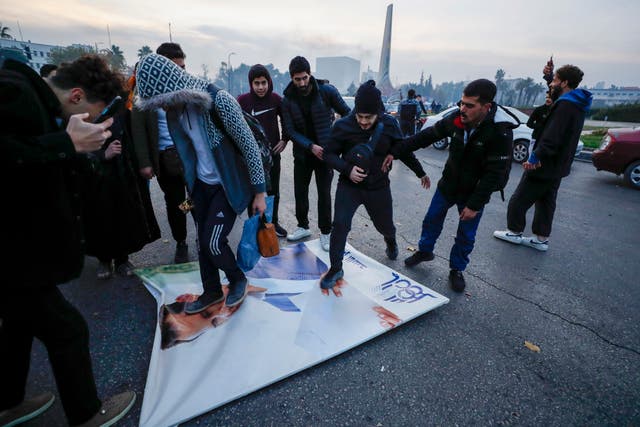 Syrians celebrate the arrival of opposition fighters as they step on a picture of Syrian President Bashar Assad in Damascus
