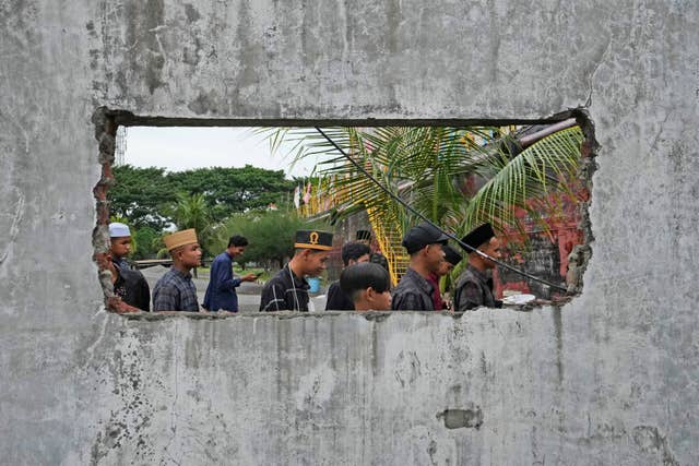 People are seen through a hole in the wall of a building damaged by the tsunami in Banda Aceh