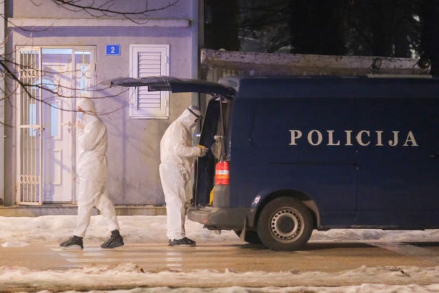 Police investigators in forensic suits beside a police van at the scene of the shooting