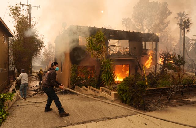 Pedestrians help a firefighter stretch a hose as an apartment building burns in Pasadena