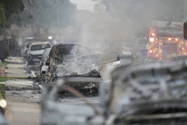 Vehicles are damaged as authorities work the scene where a small plane crashed into a San Diego neighbourhood, setting several homes on fire and forcing evacuations along several blocks early