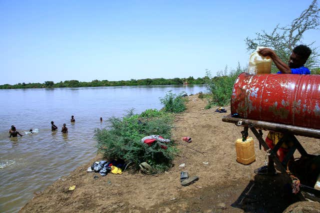 People swim in the Nile River as another person fills a water container in Khartoum
